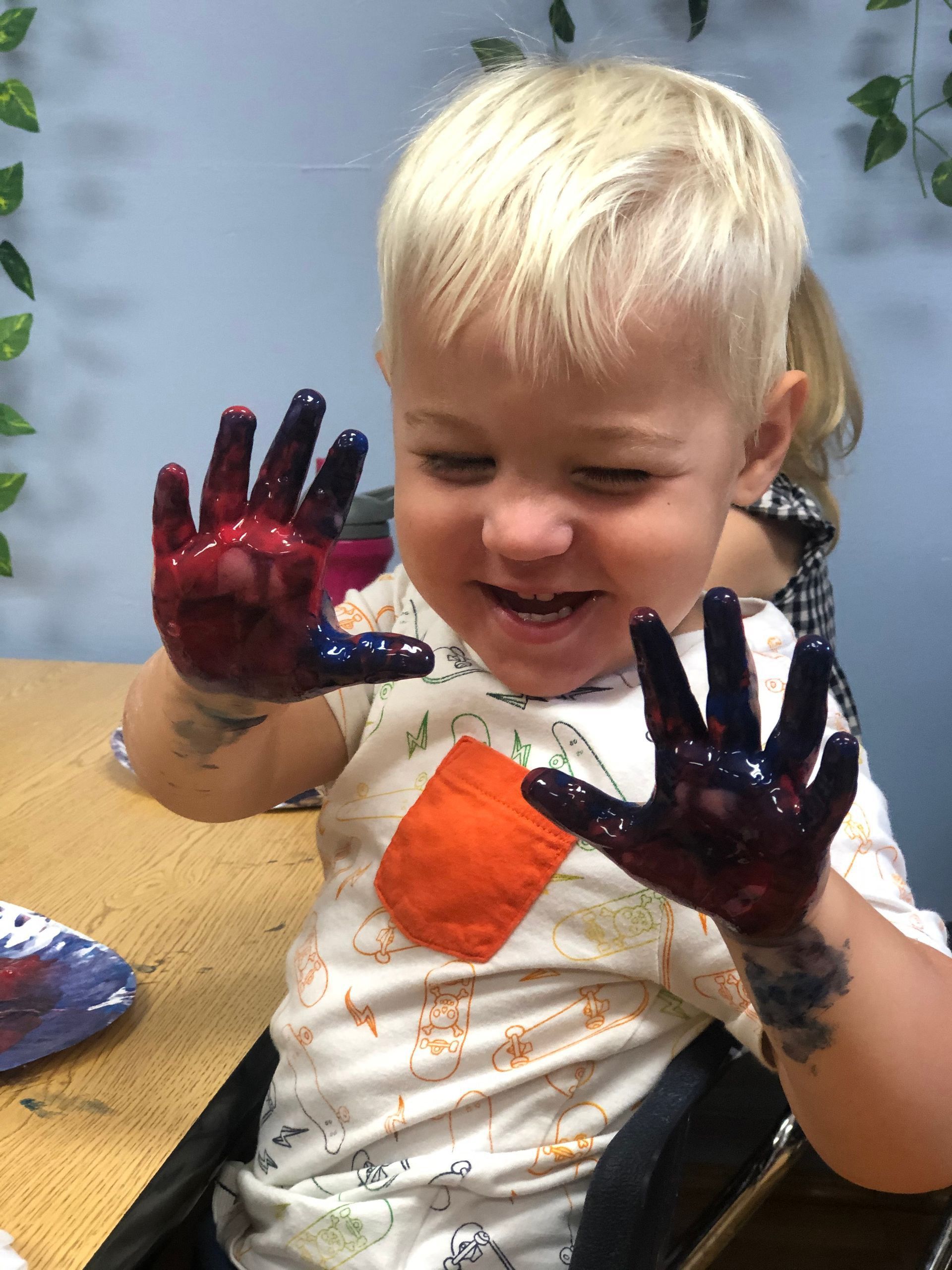 A young boy is sitting at a table with his hands covered in paint.