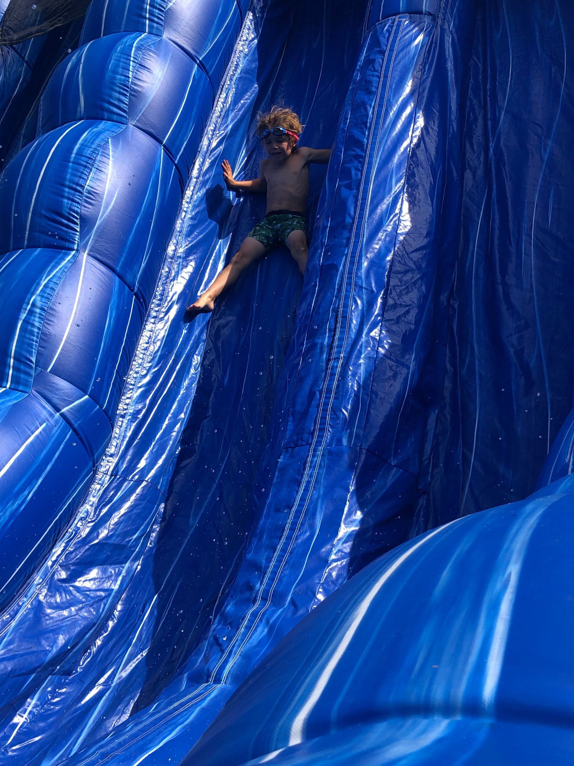 A young boy is sliding down a blue inflatable slide.