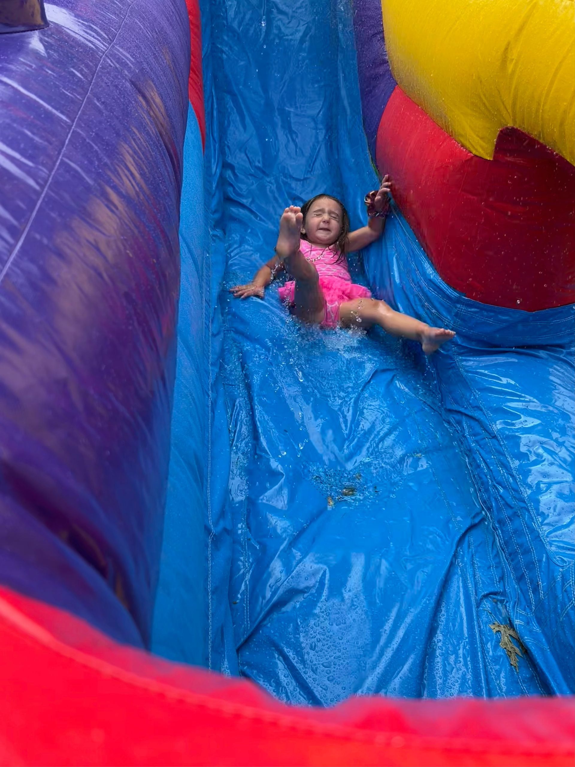 A little girl is sliding down an inflatable water slide.