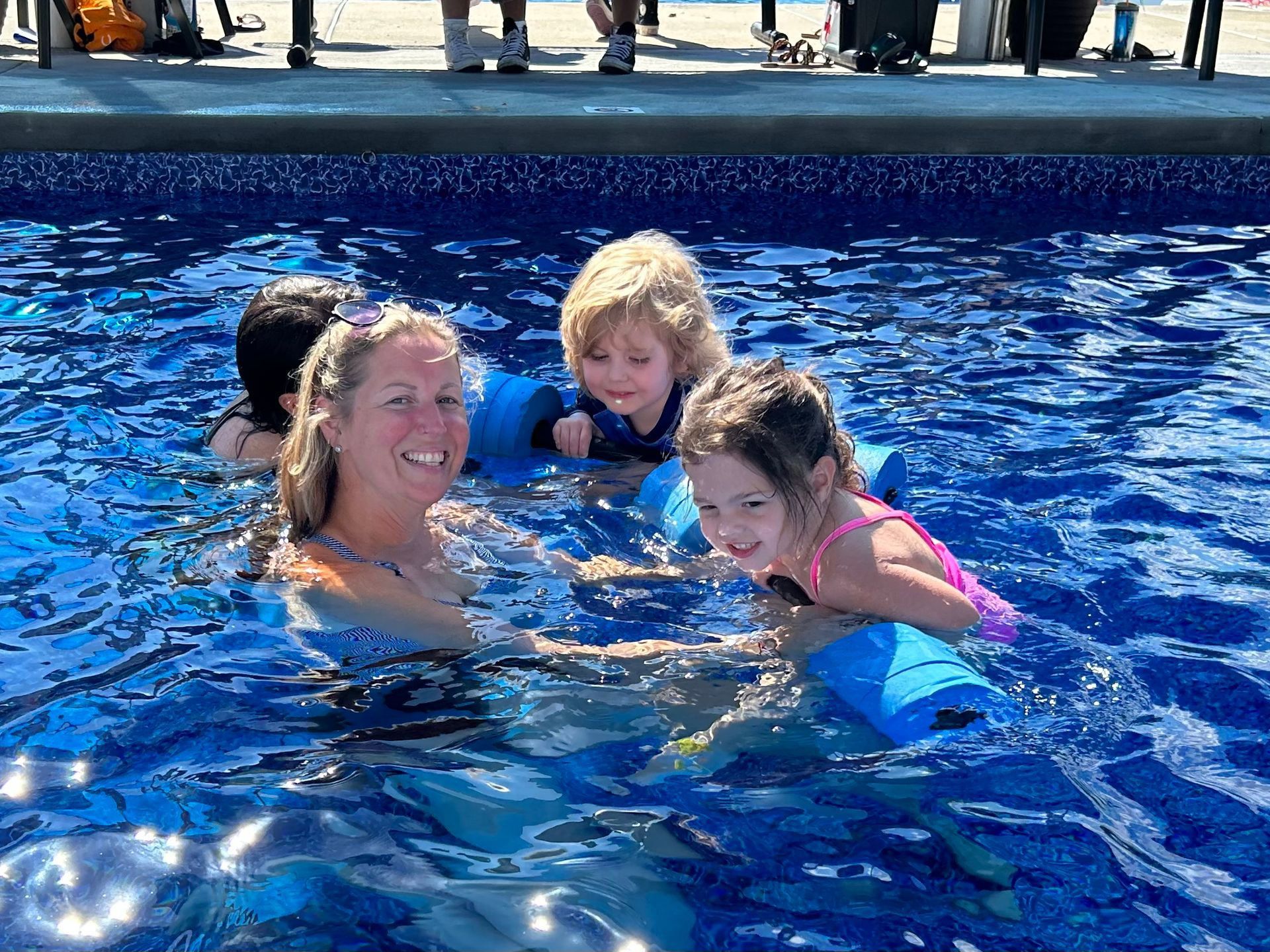 A woman and three children are swimming in a pool.