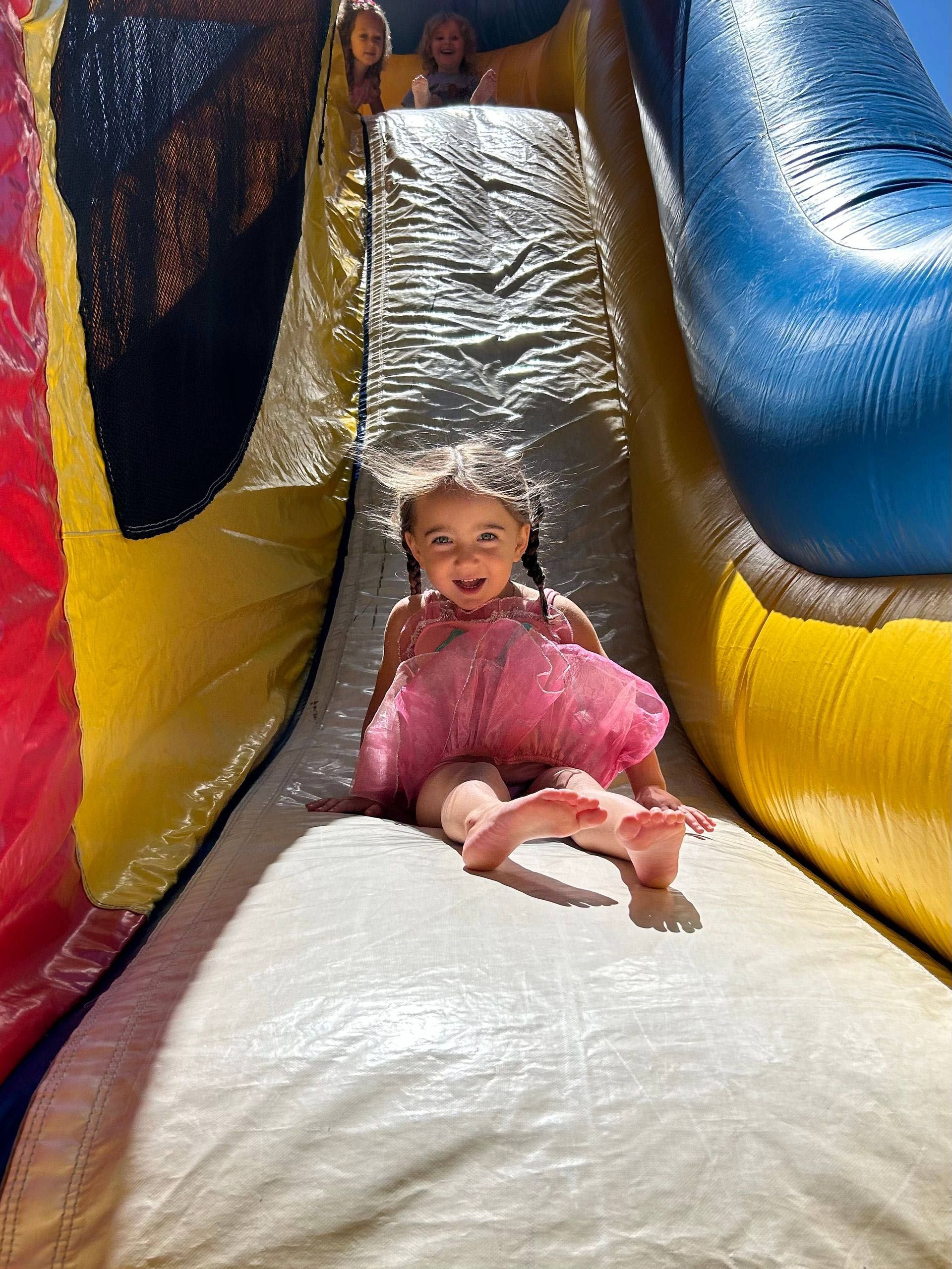 A little girl in a pink dress is sitting on top of an inflatable slide.