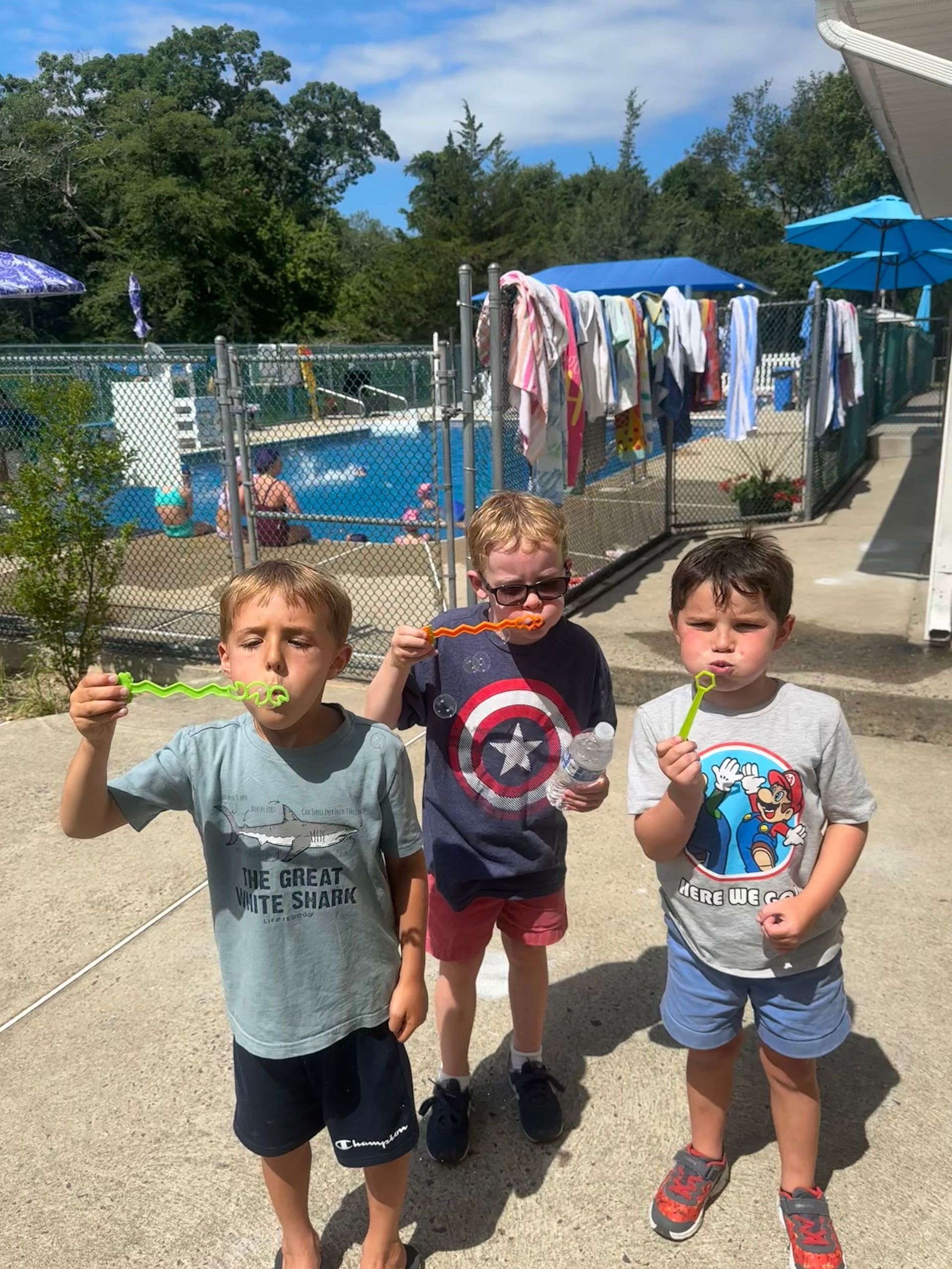 Three young boys are blowing soap bubbles in front of a pool.