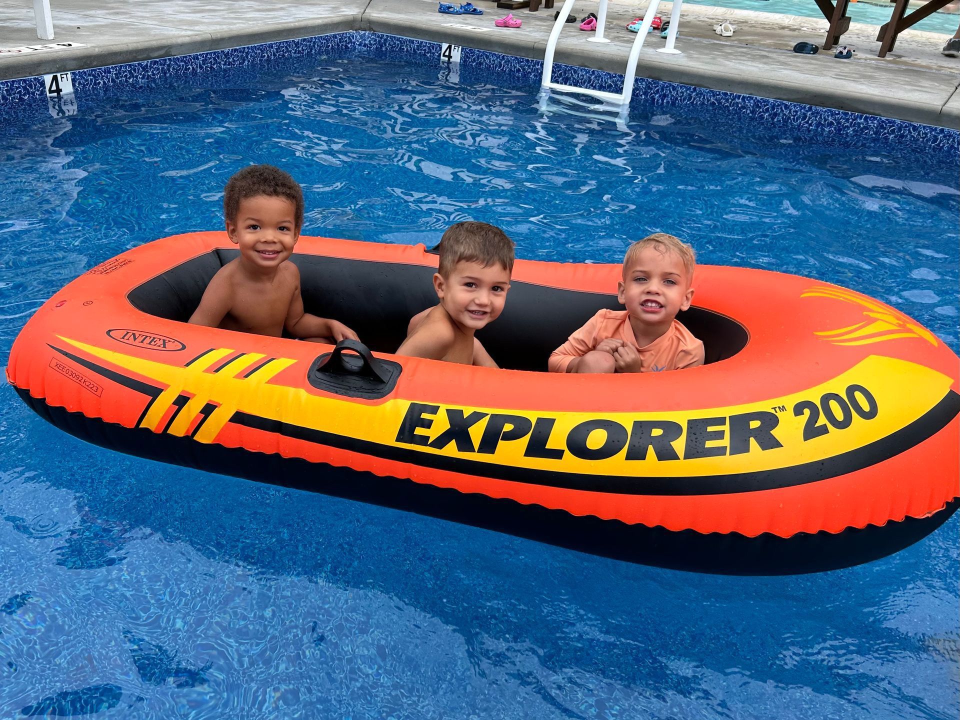 Three children are sitting in an inflatable boat in a swimming pool.