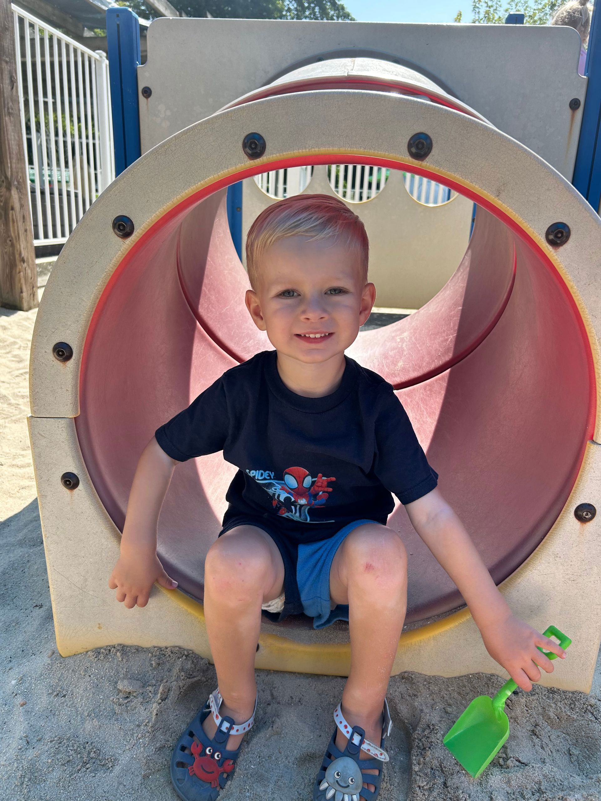 A young boy is sitting in a tunnel at a playground.