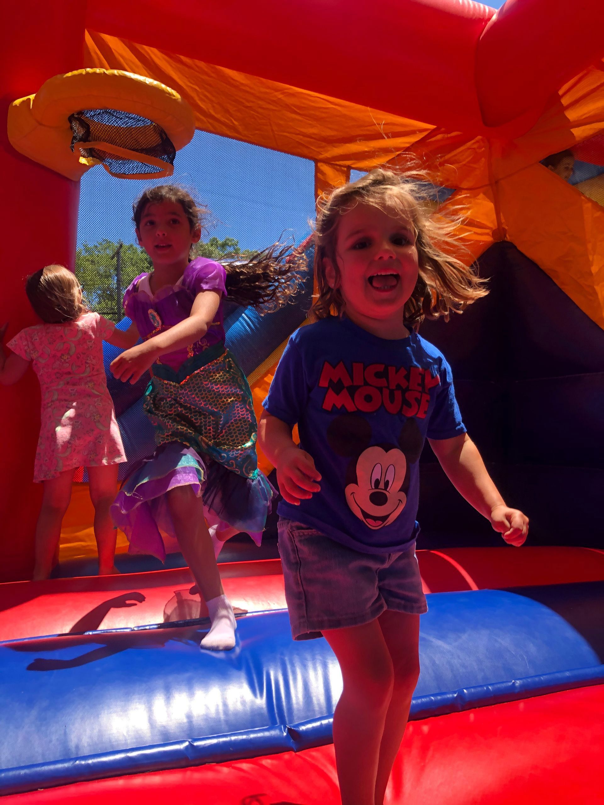 A little girl wearing a mickey mouse shirt is jumping in a bouncy house.