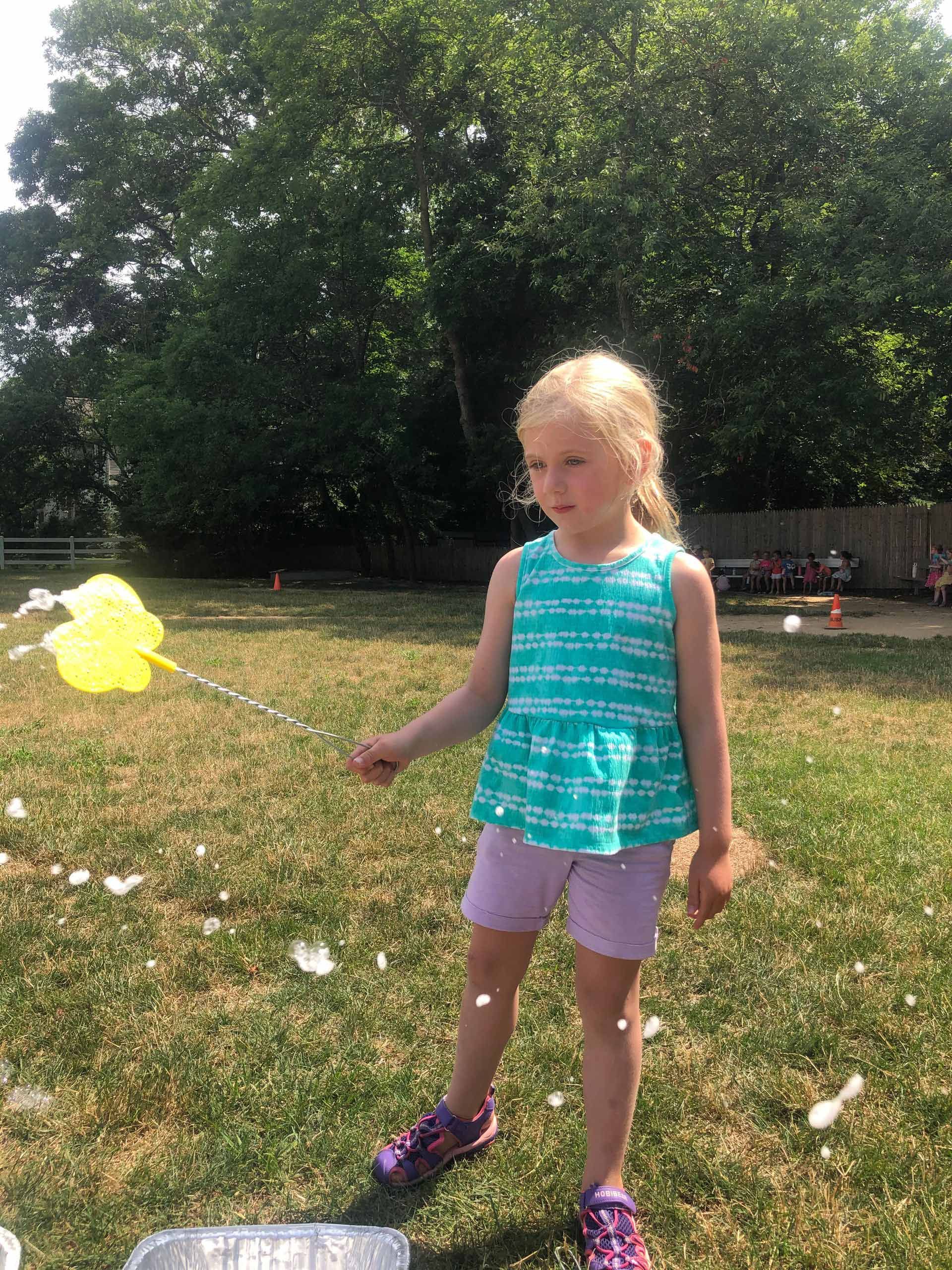 A little girl is playing with soap bubbles in a park.