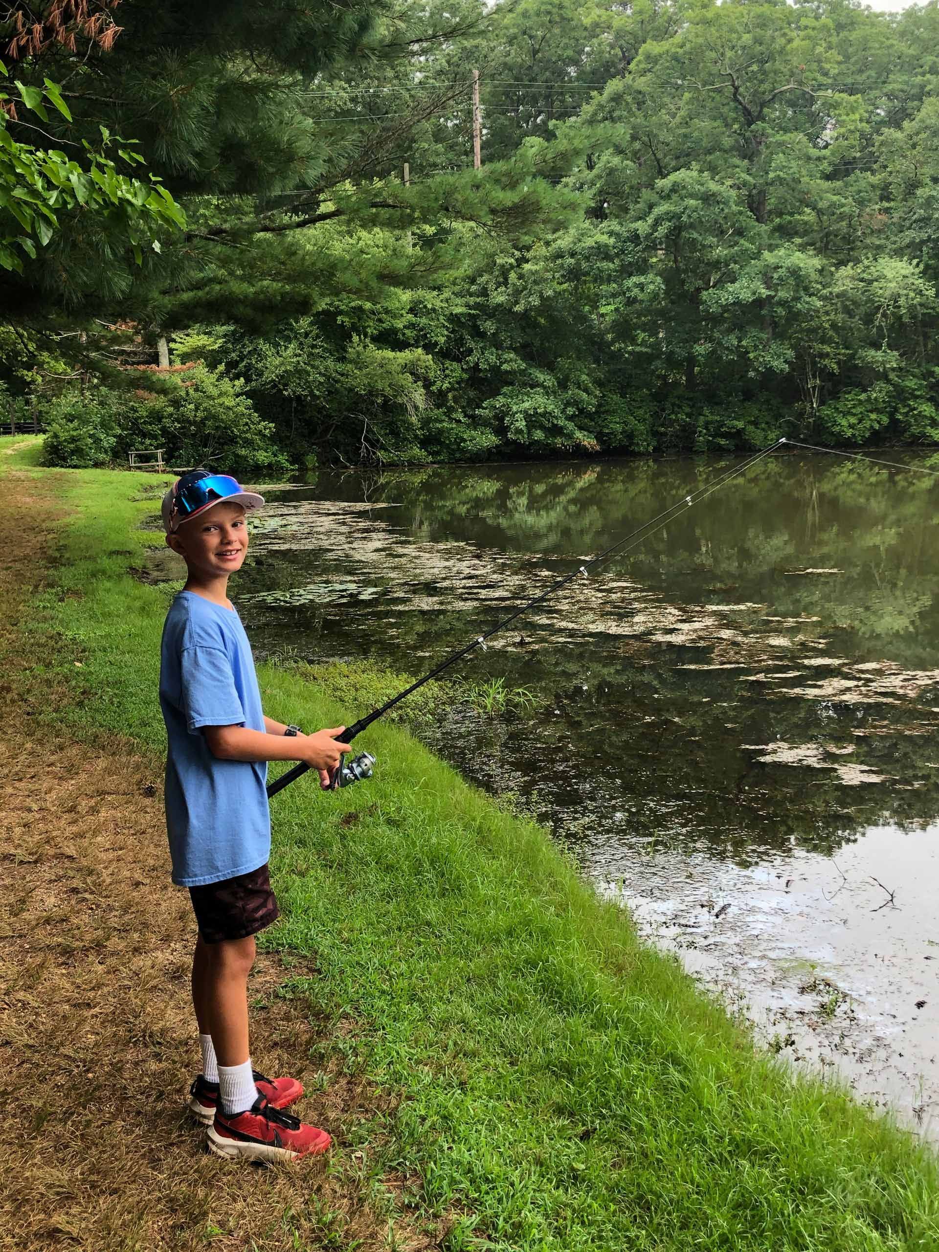 A young boy is fishing in a pond with a fishing rod.