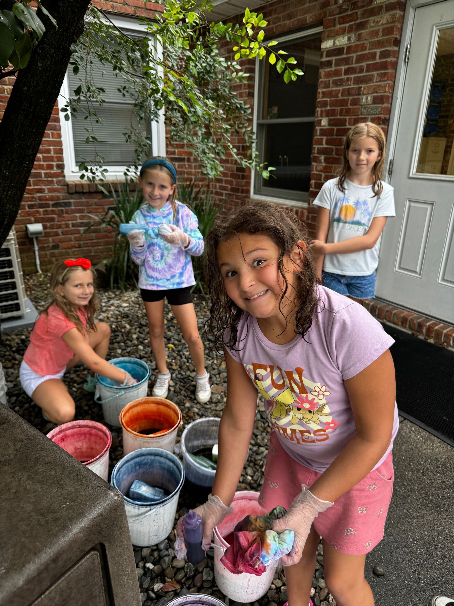 A group of young girls are making tie dye outside of a brick house.