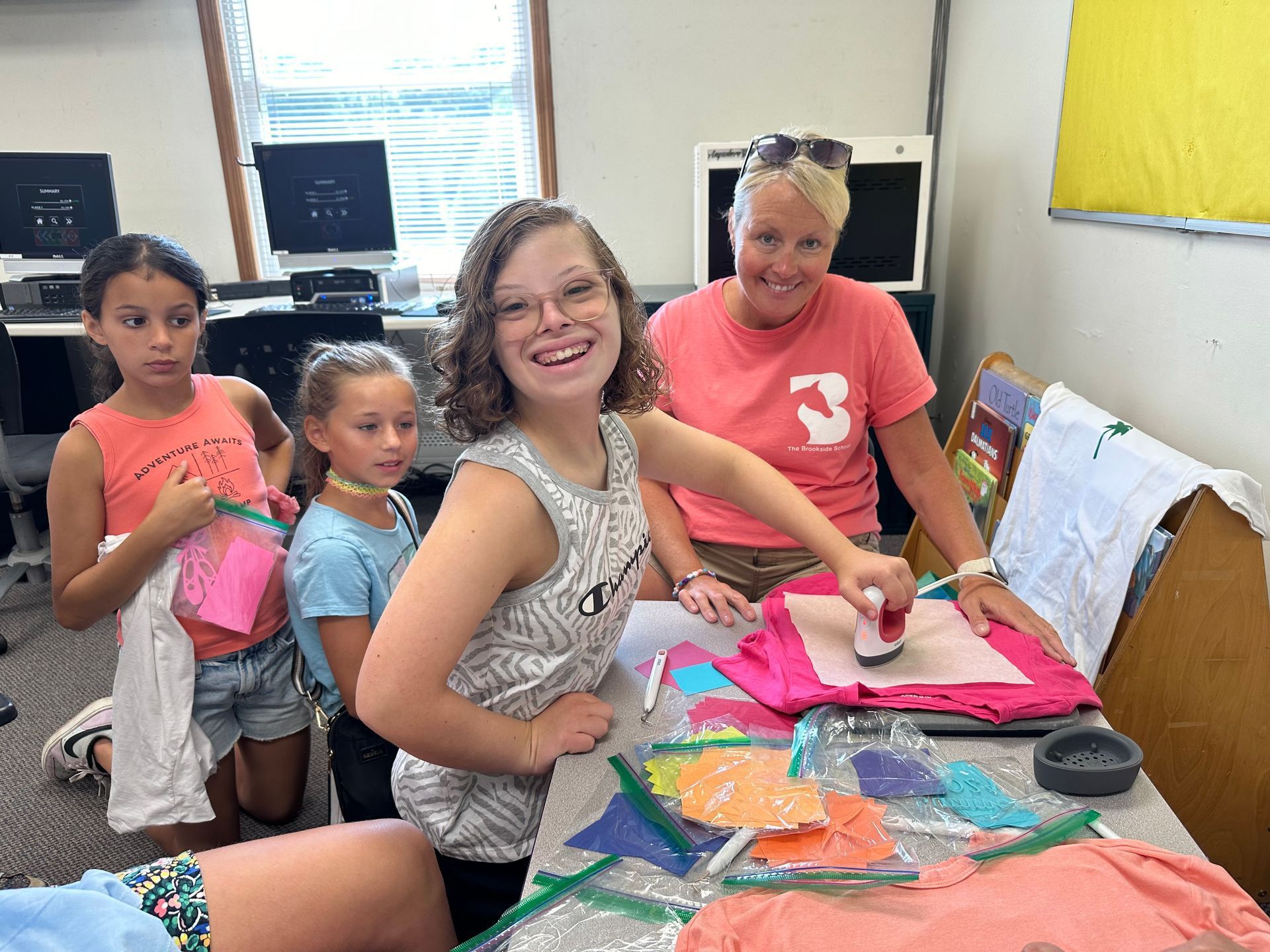 A group of young girls are sitting at a table with a woman in a pink shirt with the number 3 on it.