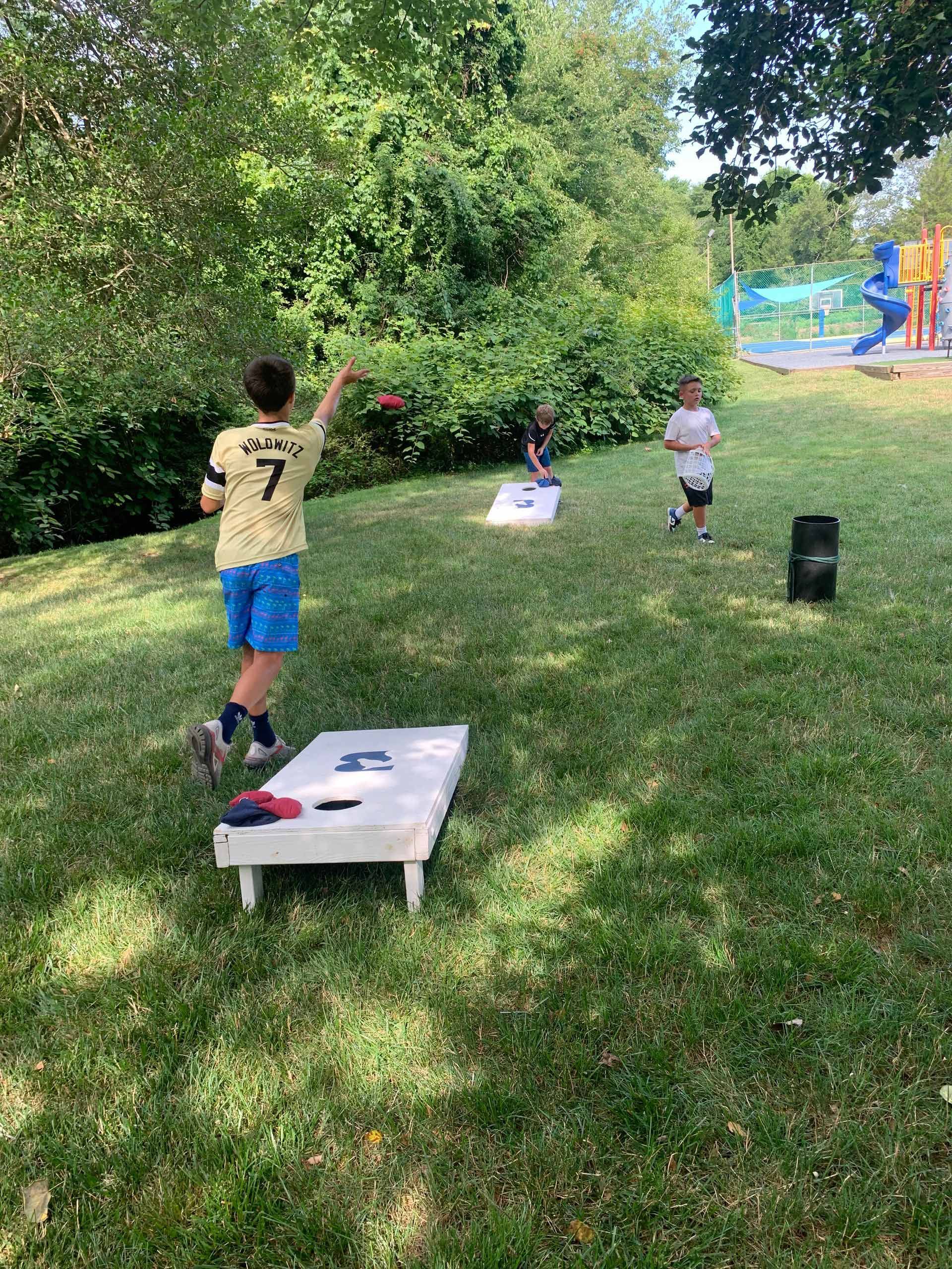 A group of children are playing cornhole in a park.