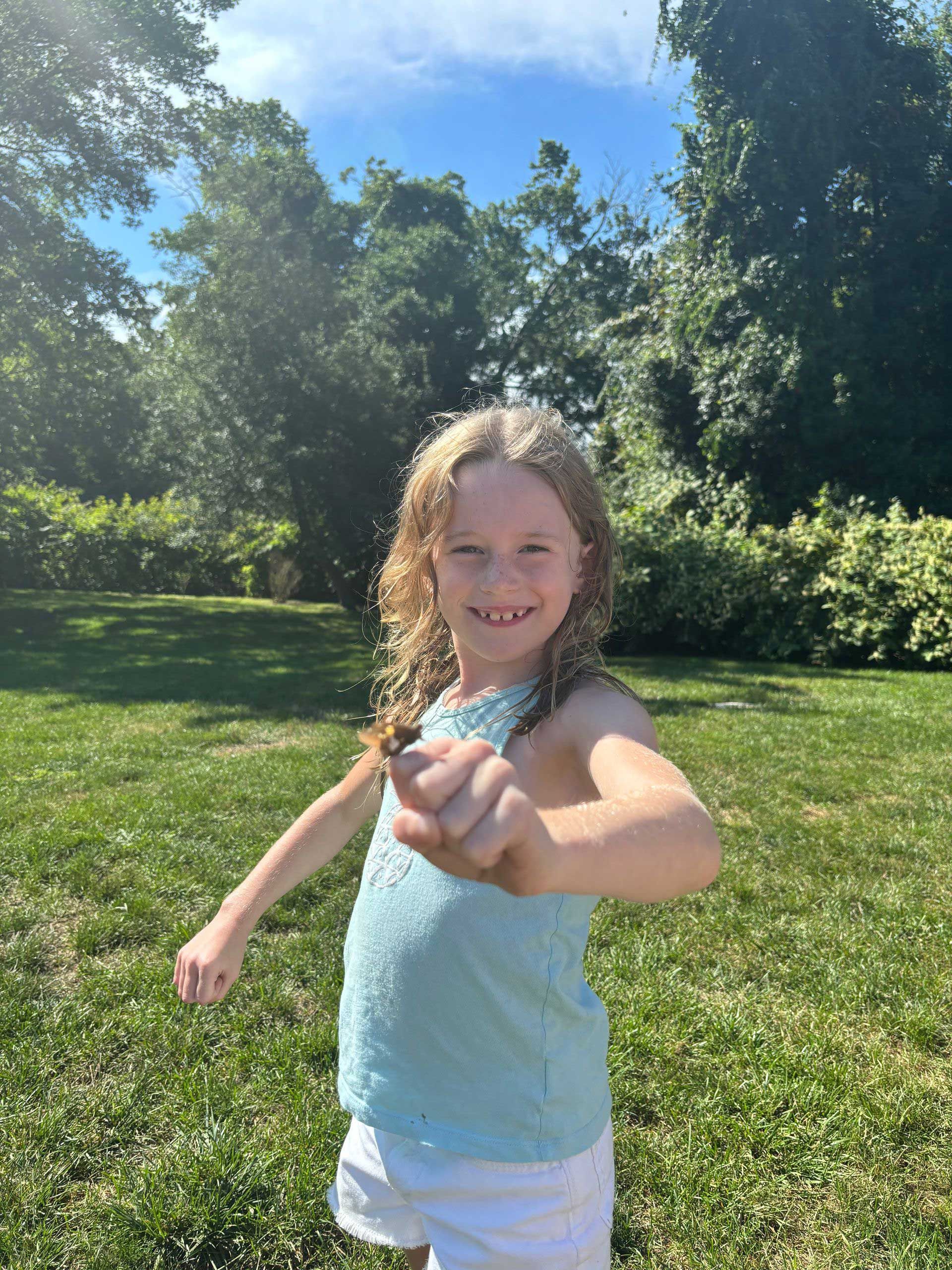 A young girl is standing in a grassy field giving a thumbs up.