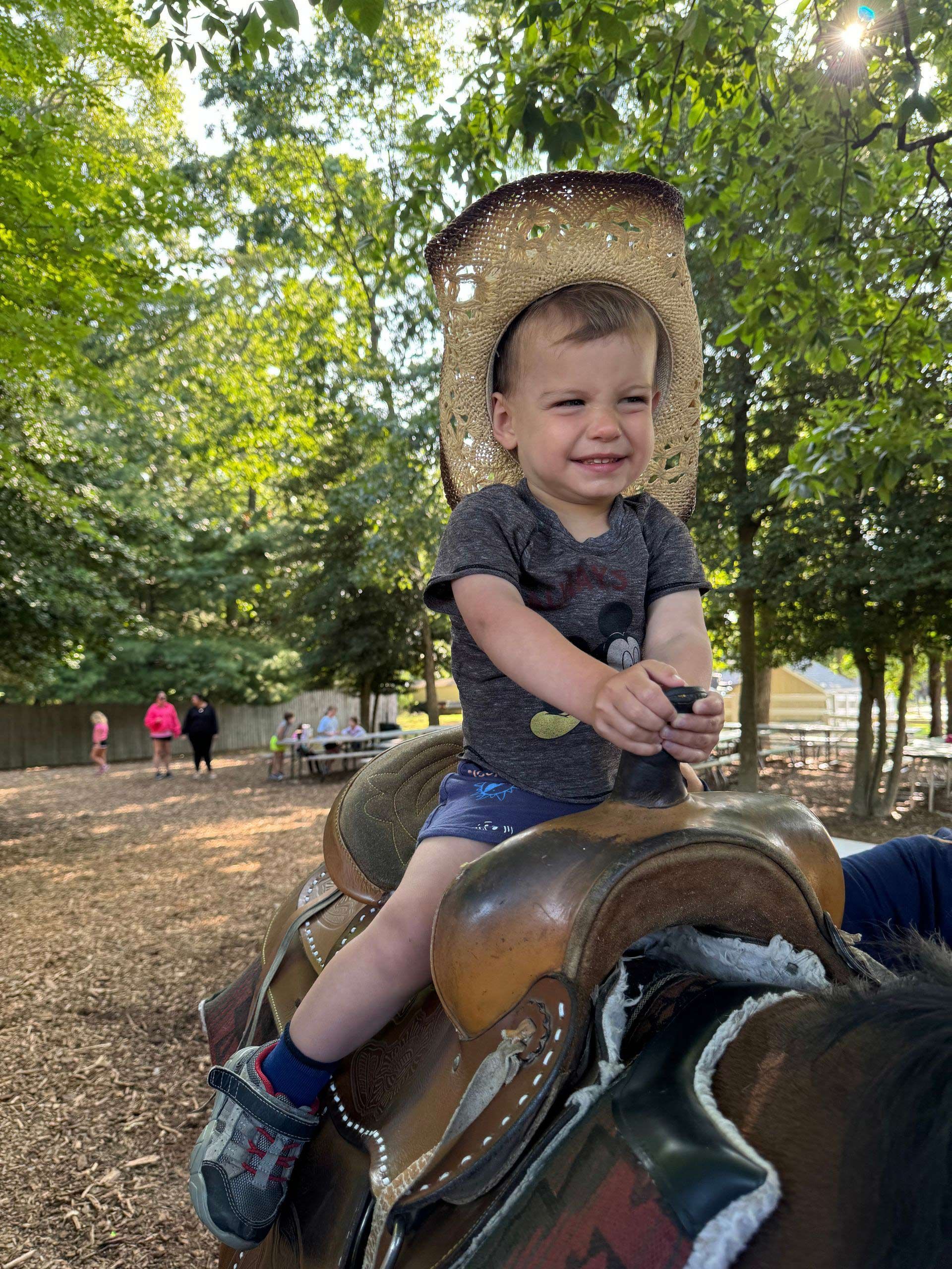 A little boy wearing a cowboy hat is sitting on a saddle.