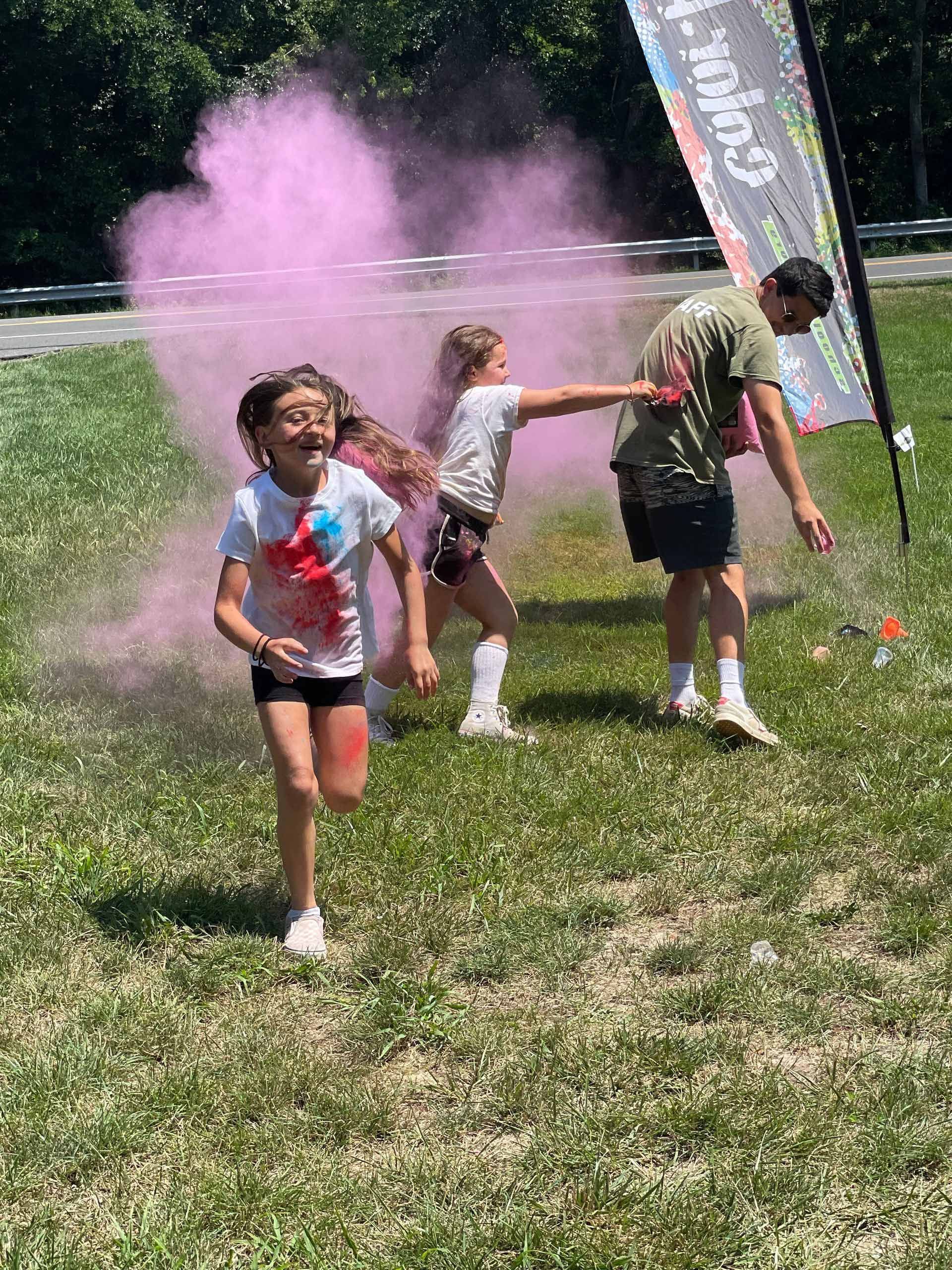 A group of children are running through a field of pink powder.