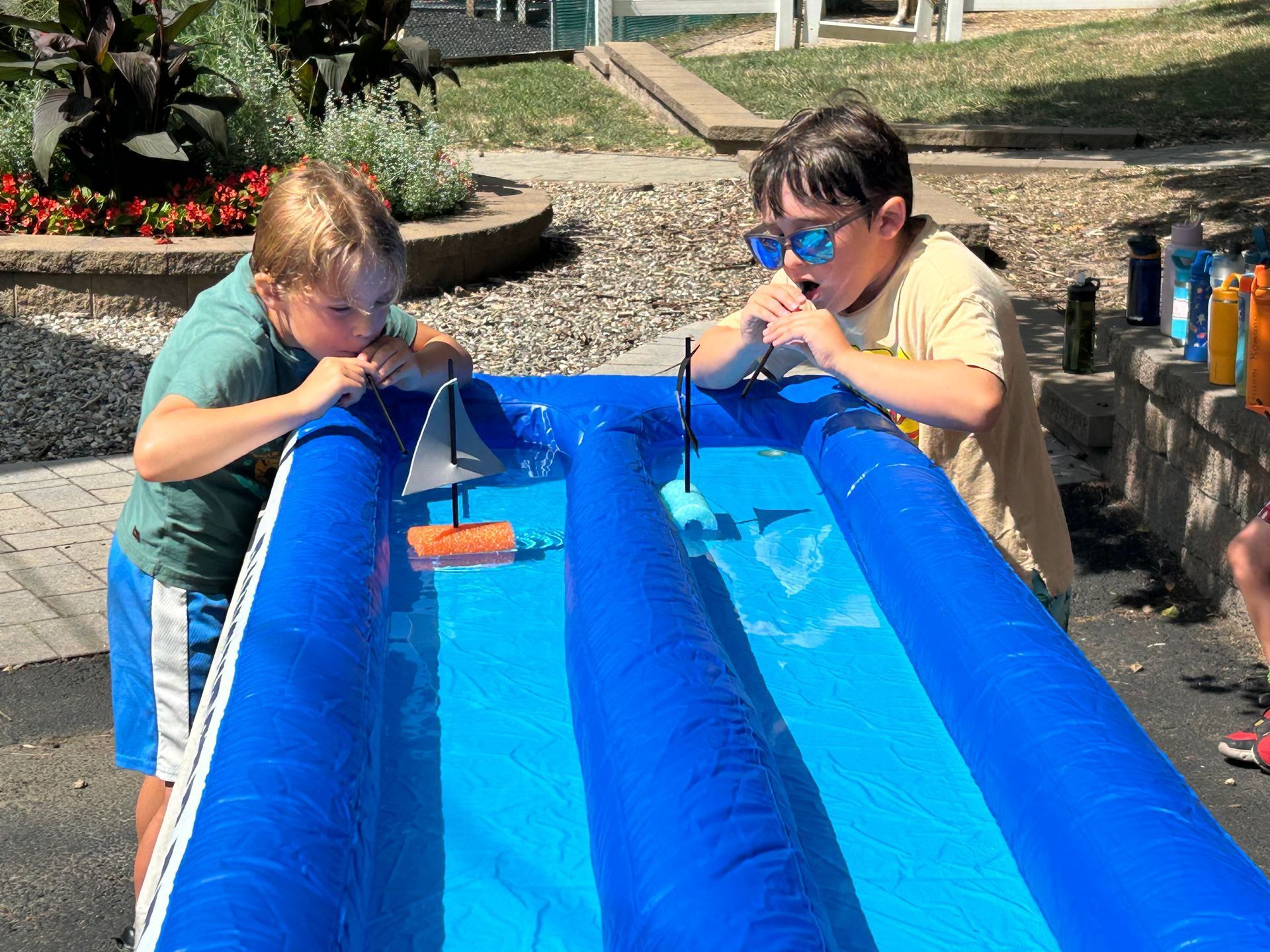 Two young boys are playing with boats in an inflatable pool.