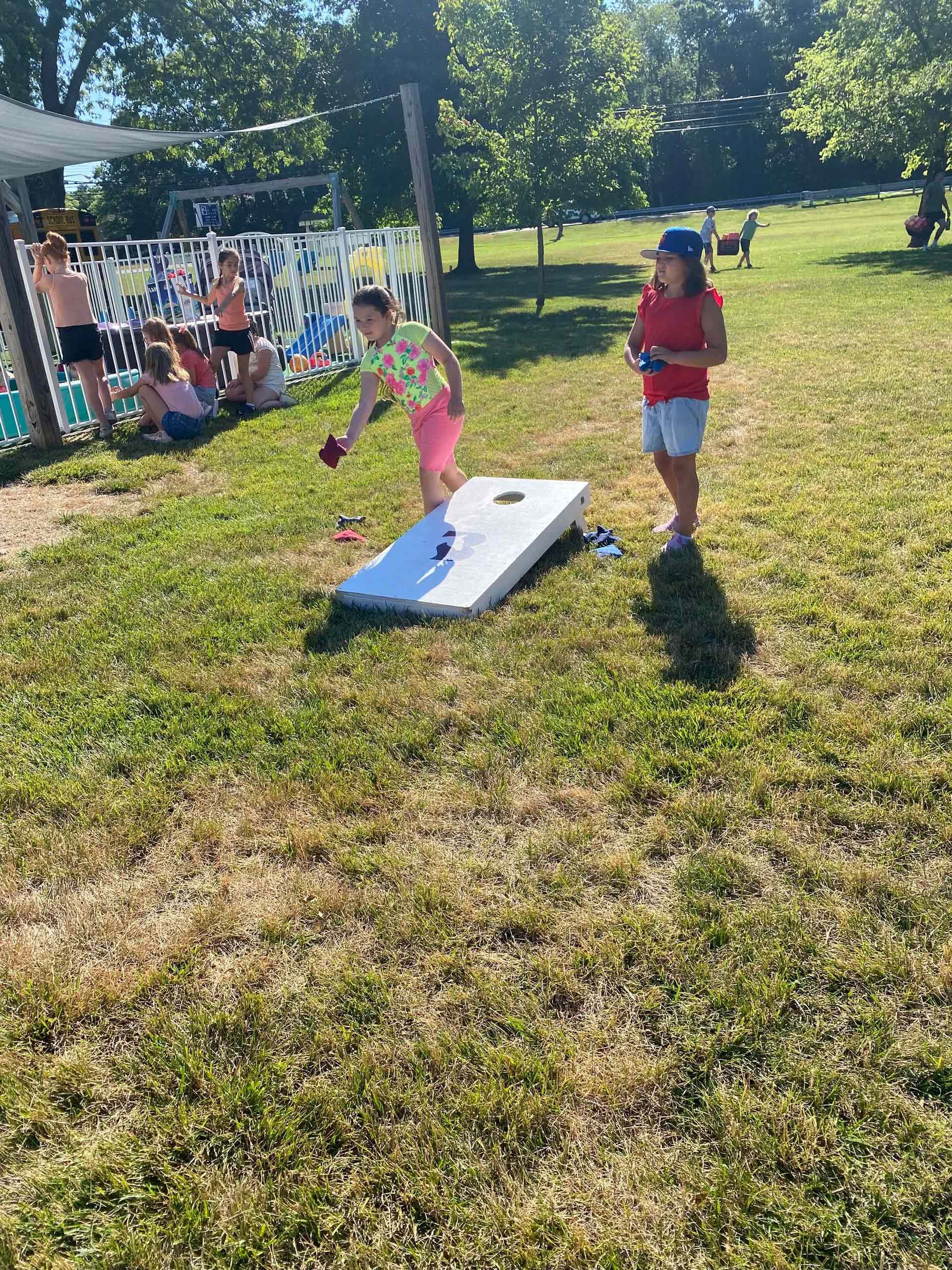 Two young girls are playing cornhole in a park.