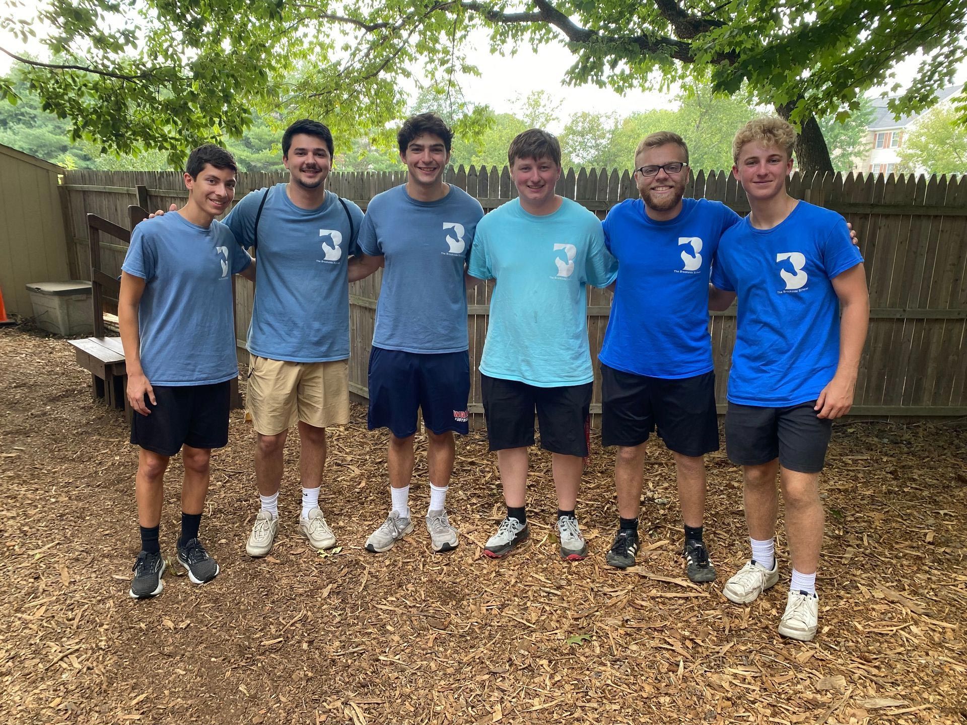 A group of young men are posing for a picture in front of a wooden fence.