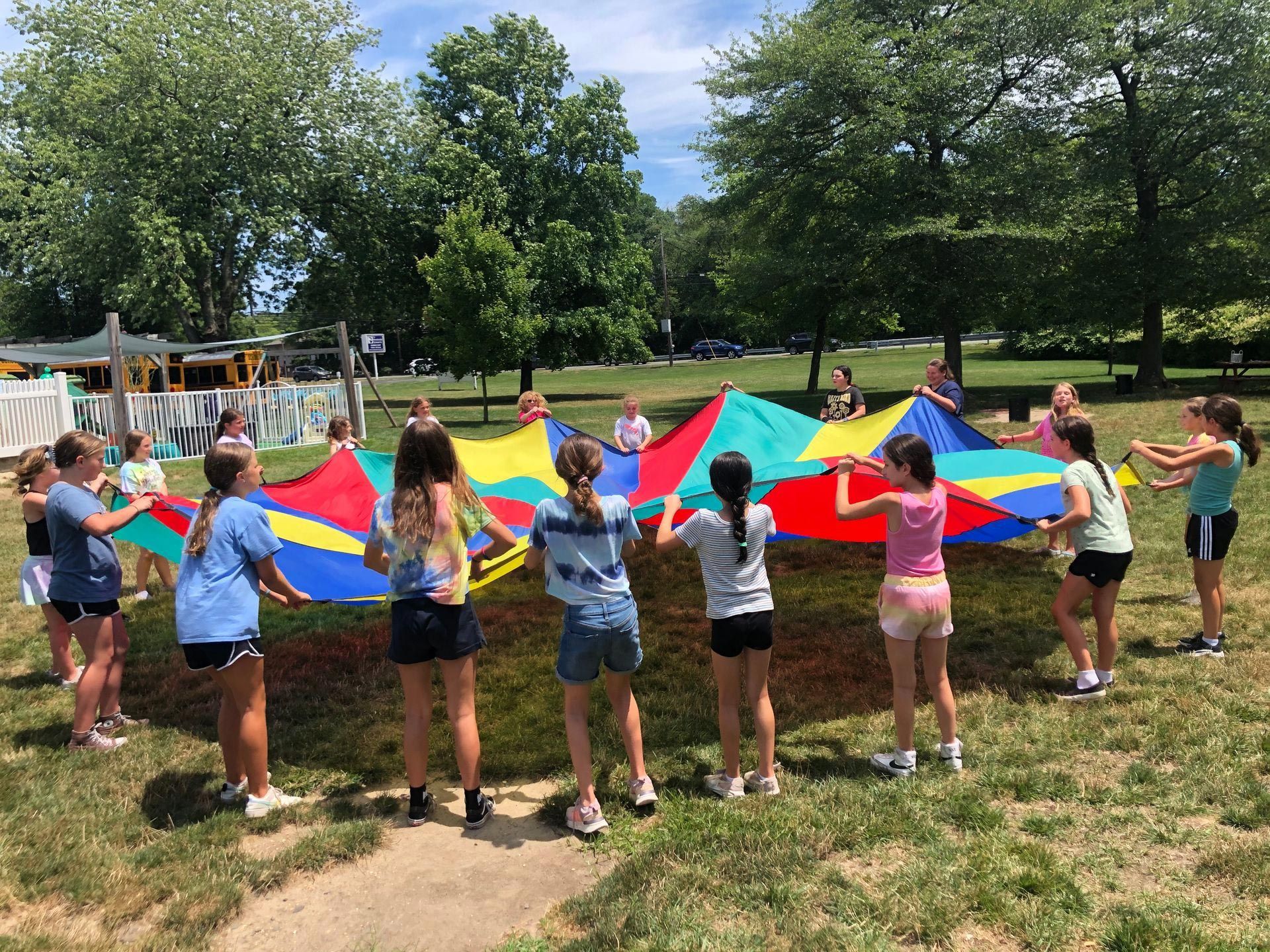 A group of young girls are holding a colorful parachute in a park.