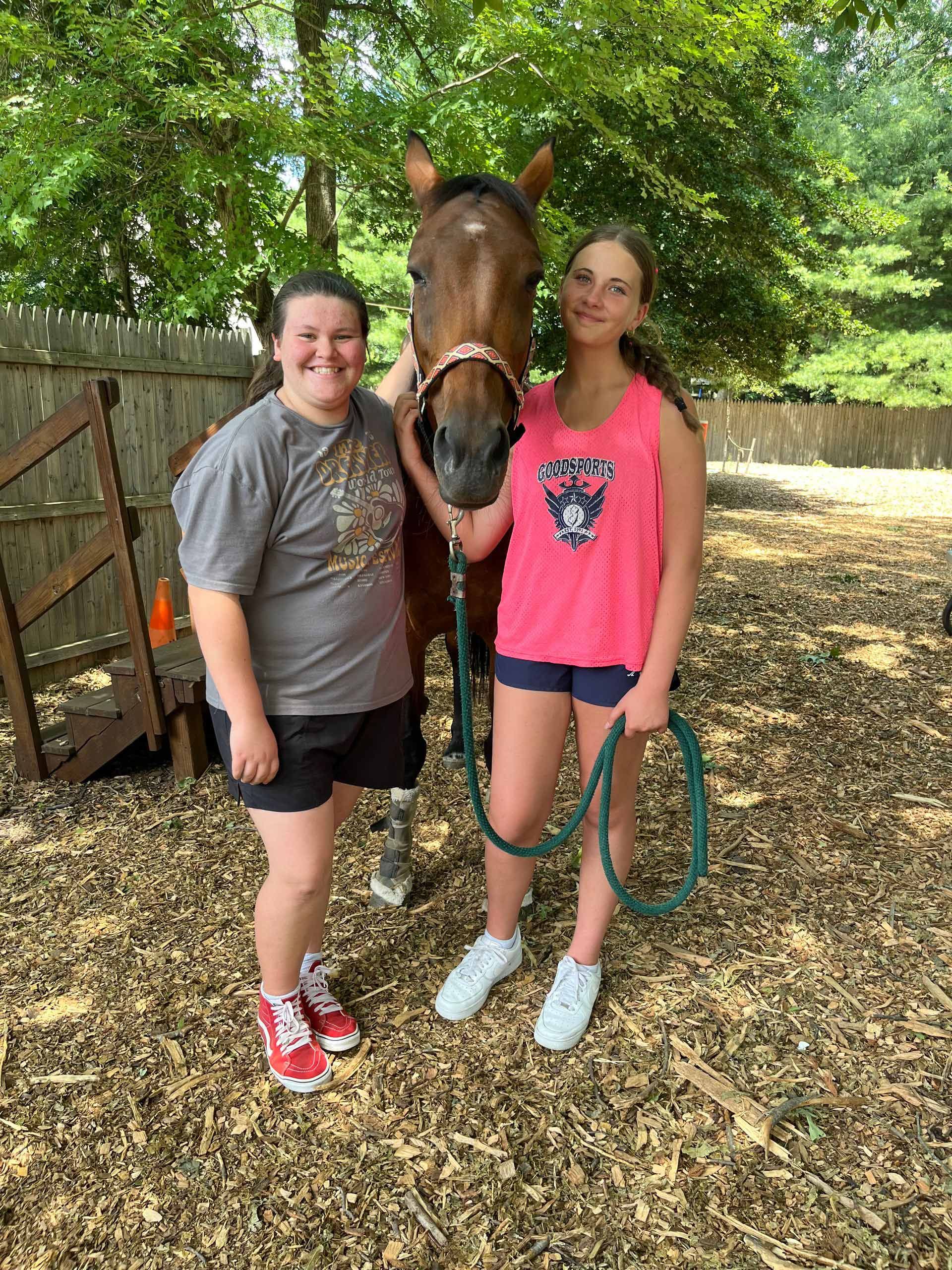 Two girls are standing next to a horse on a leash.