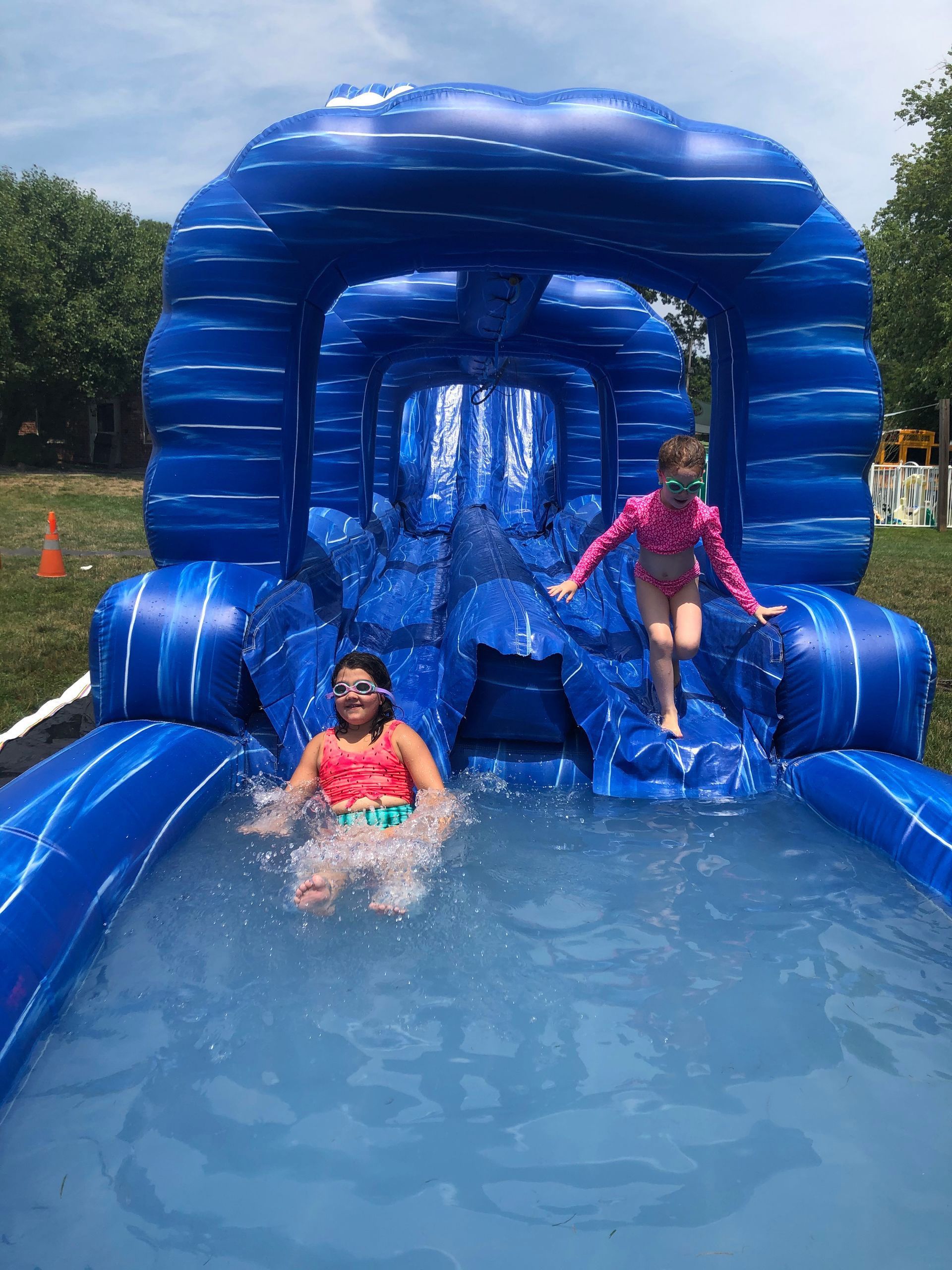 Two girls are playing on an inflatable water slide.