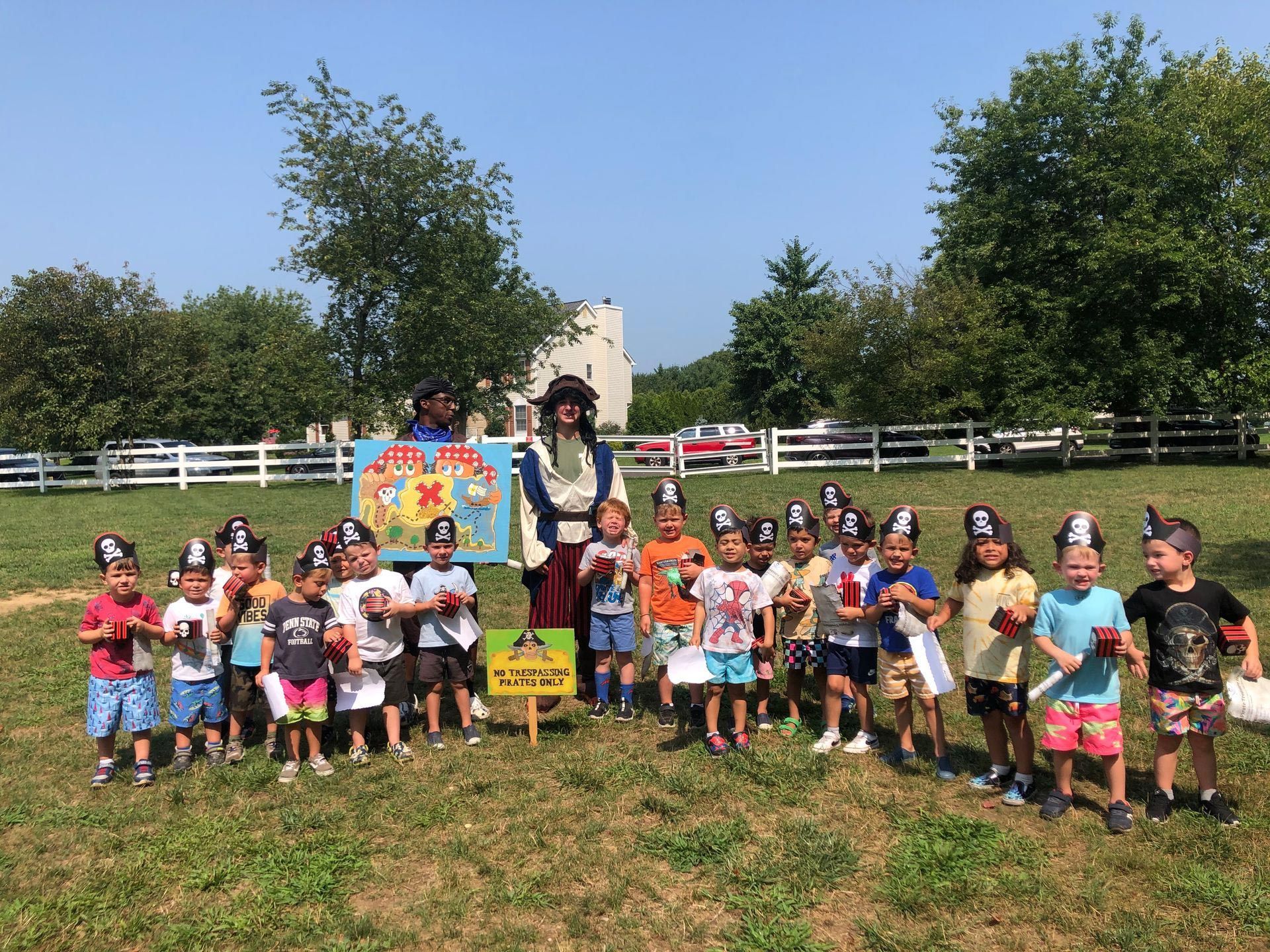 A group of children wearing pirate hats are standing in a field.