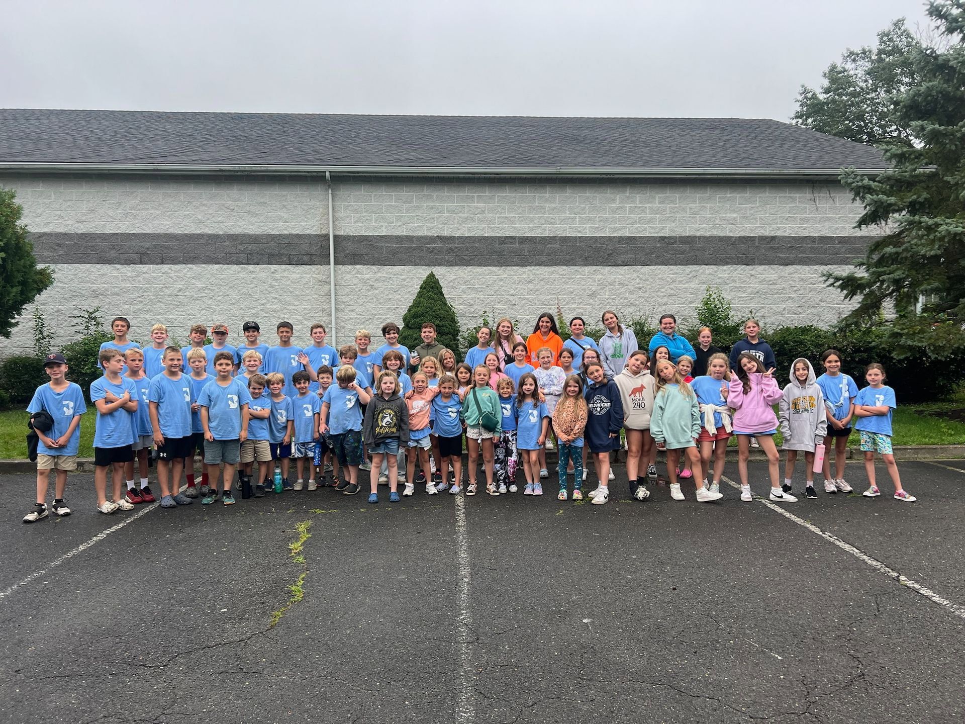 A large group of children are posing for a picture in a parking lot.