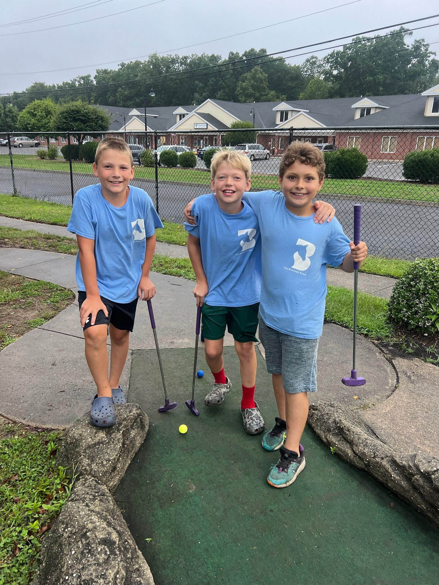 Three young boys are playing mini golf on a sidewalk.