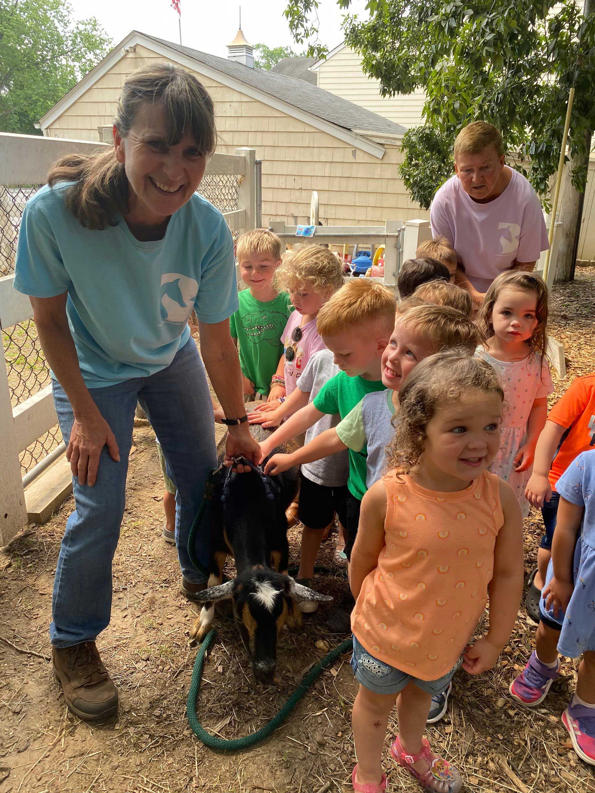 A woman is standing next to a group of children holding a goat on a leash.