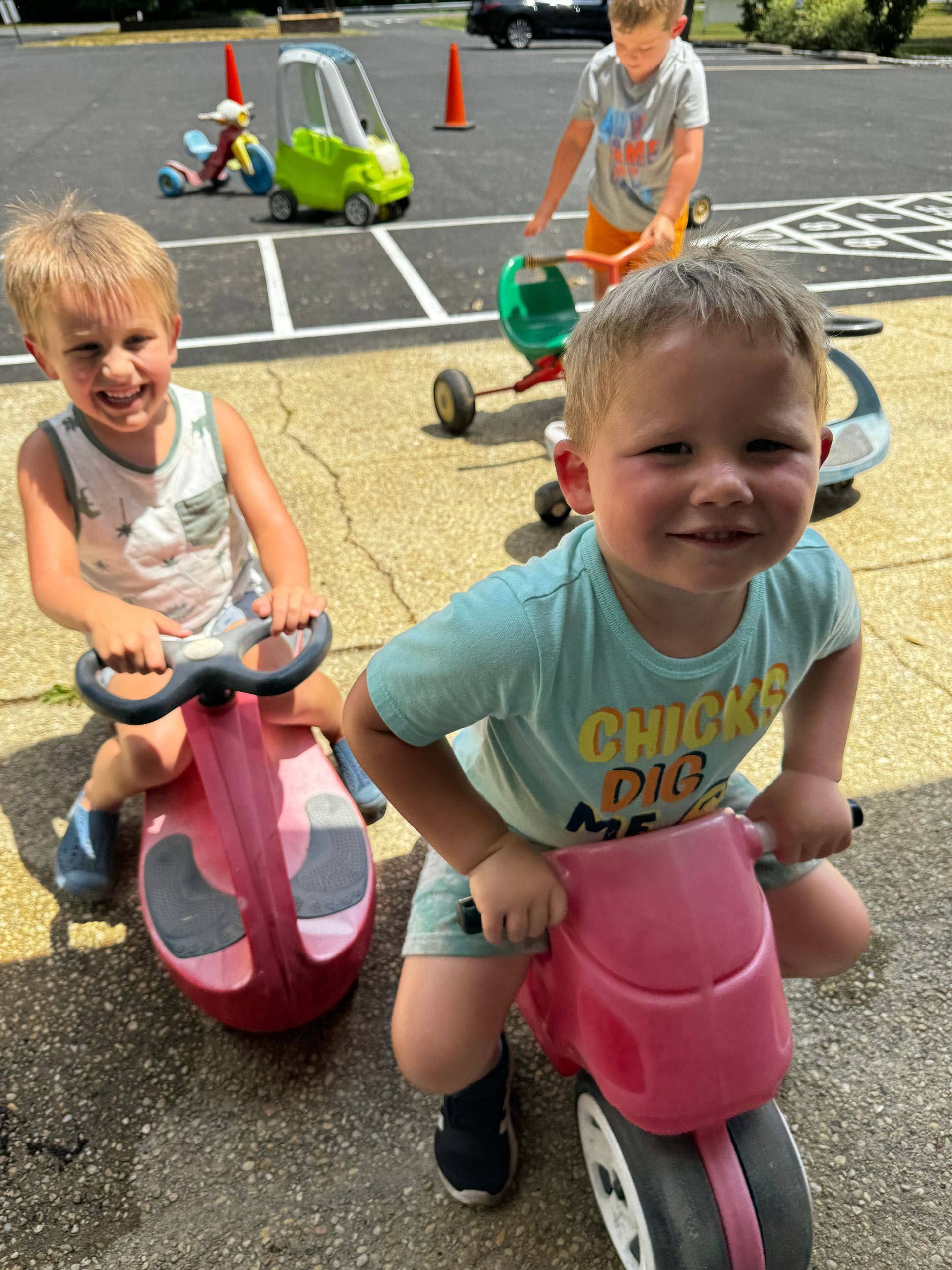 Three young boys are playing with toys in a parking lot.