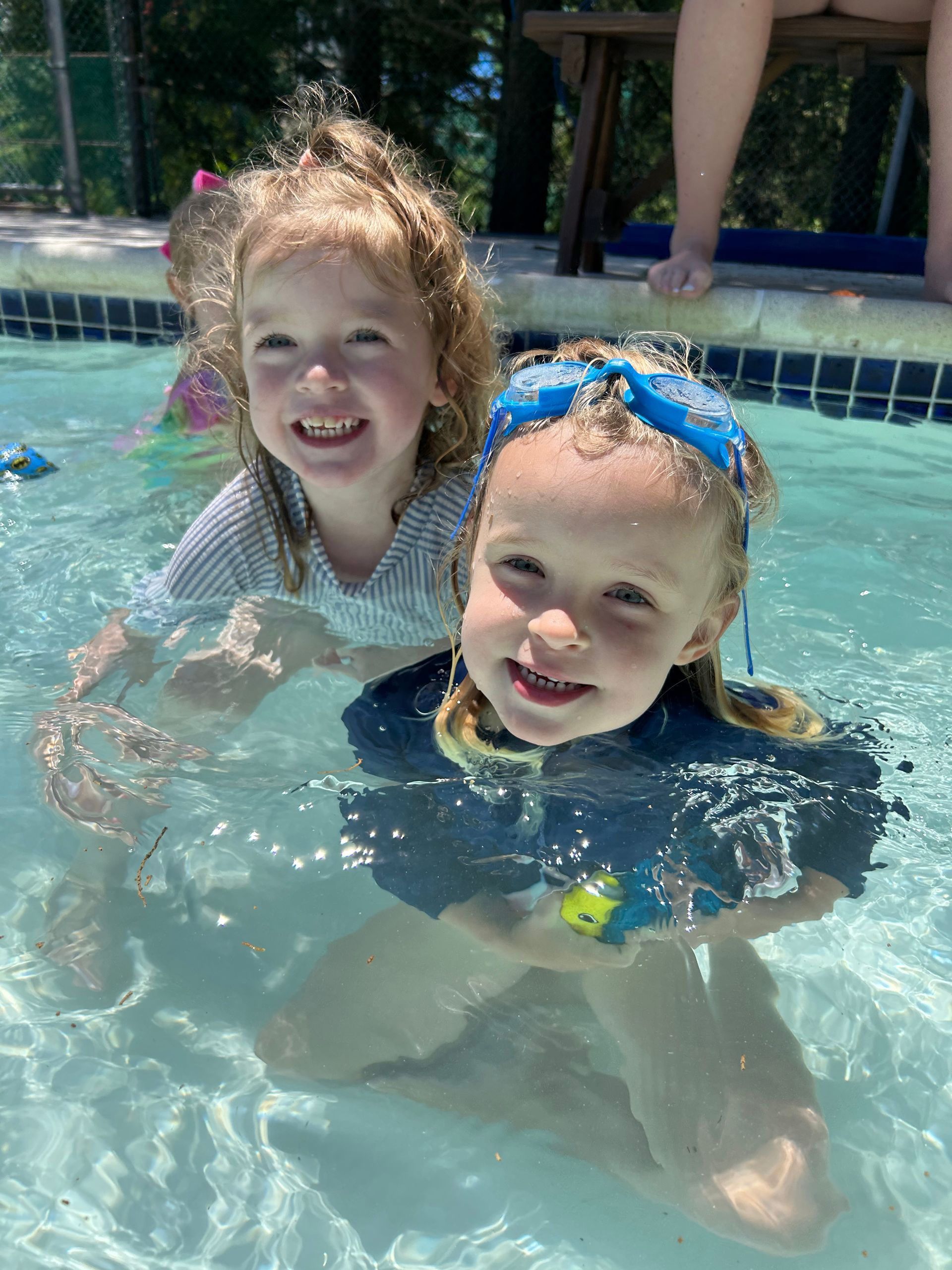 Two little girls are swimming in a pool and smiling for the camera.