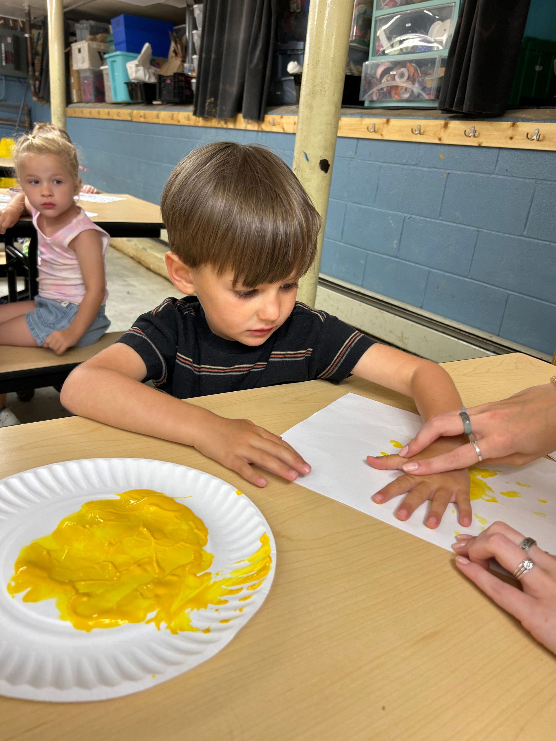 A young boy is sitting at a table painting his hands with yellow paint.