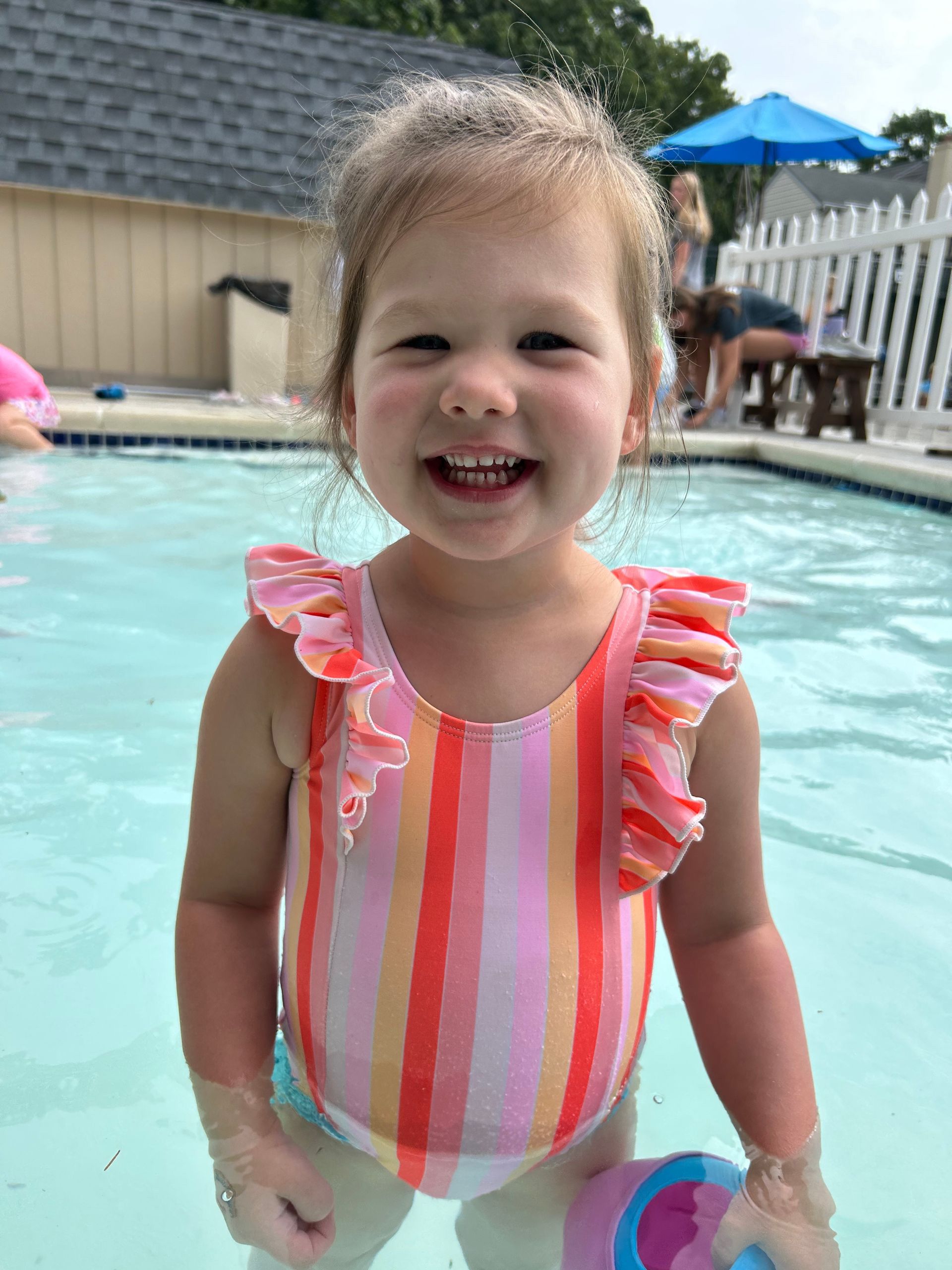 A little girl in a striped bathing suit is standing in a swimming pool.