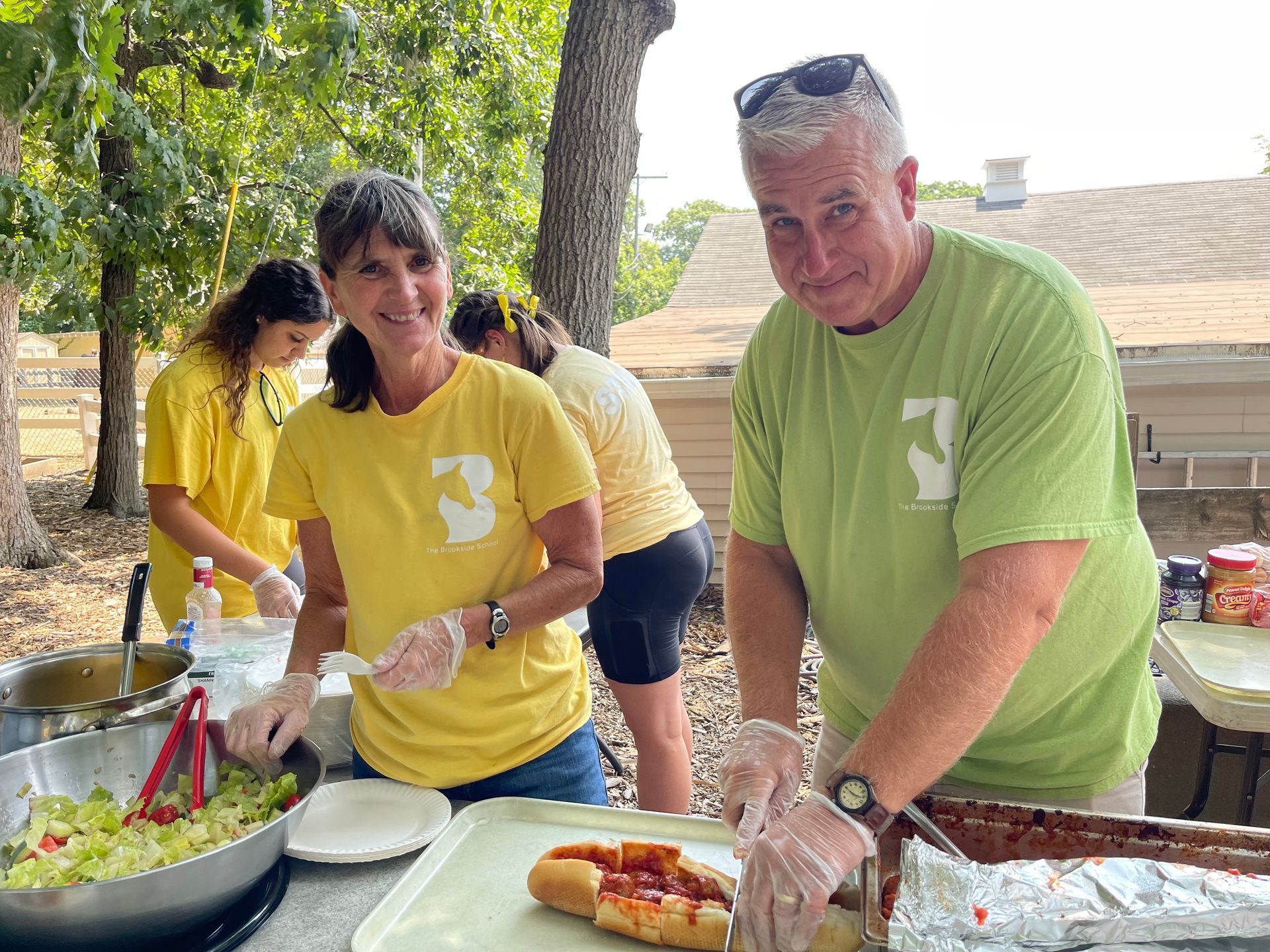 A man and a woman are preparing food at a picnic table.