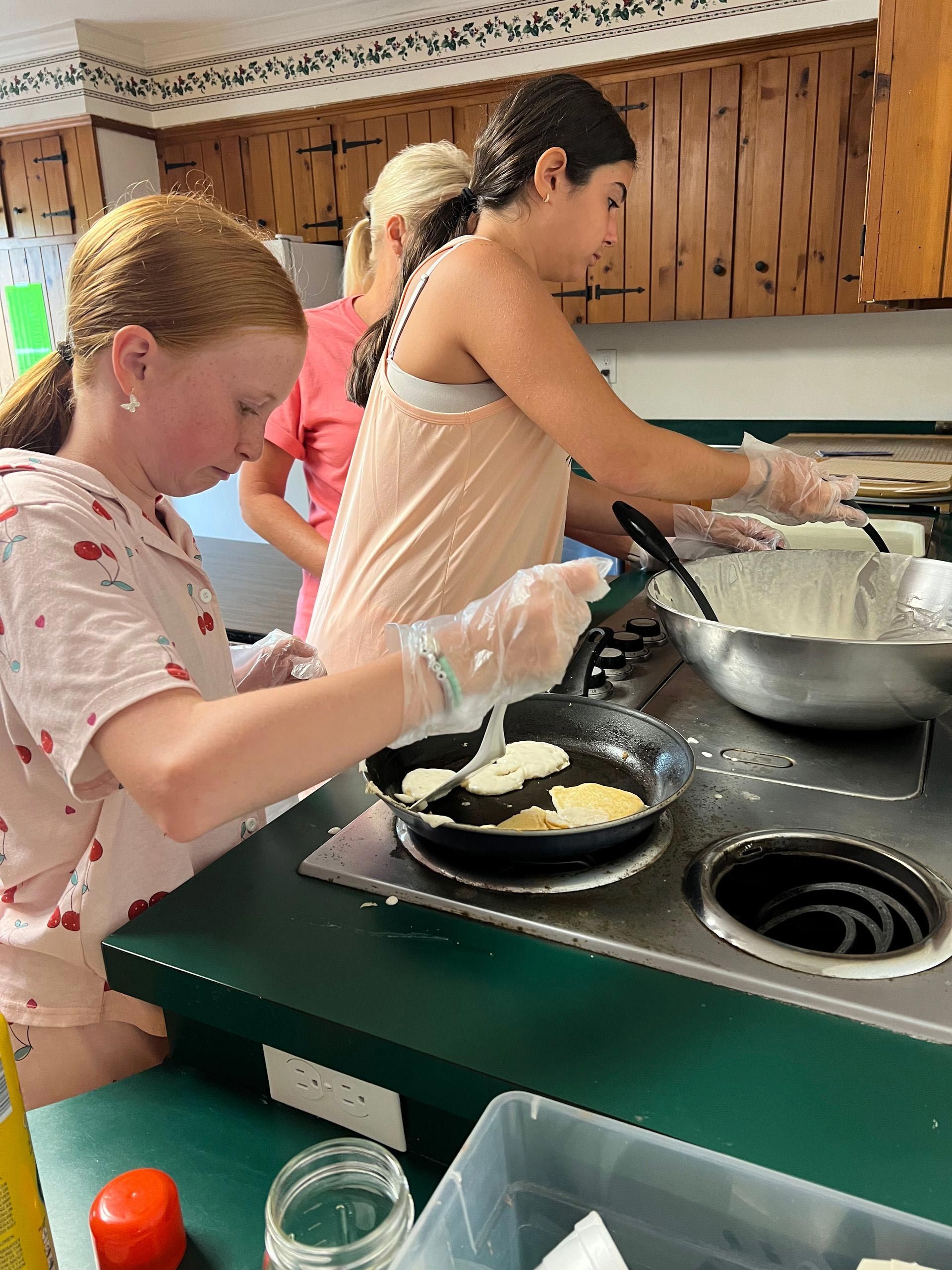 A group of young girls are cooking pancakes in a kitchen.