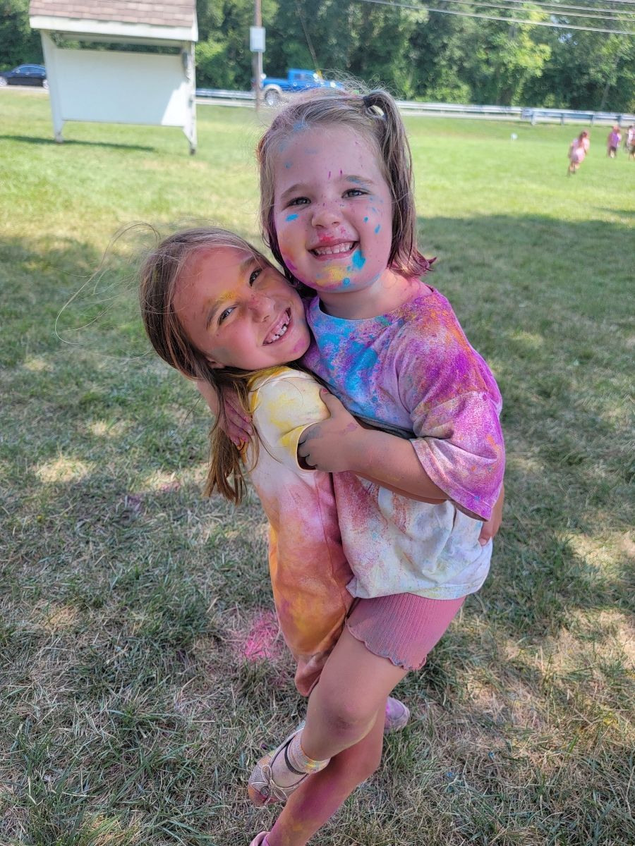 Two little girls are hugging each other in a field.