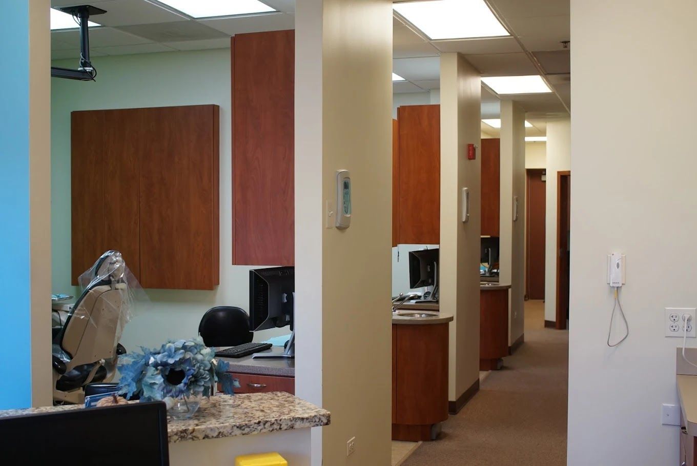 Hallway in dental office with beige walls, brown cabinets, and workstation.