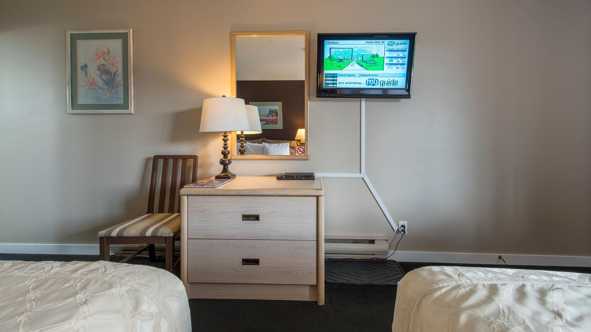 A hotel room with two beds , a dresser , a mirror and a flat screen tv.