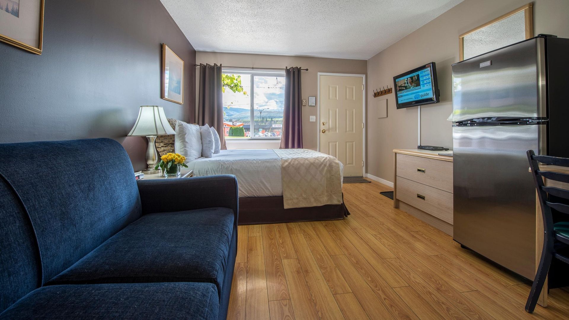 A hotel room with a couch , bed , refrigerator and television.