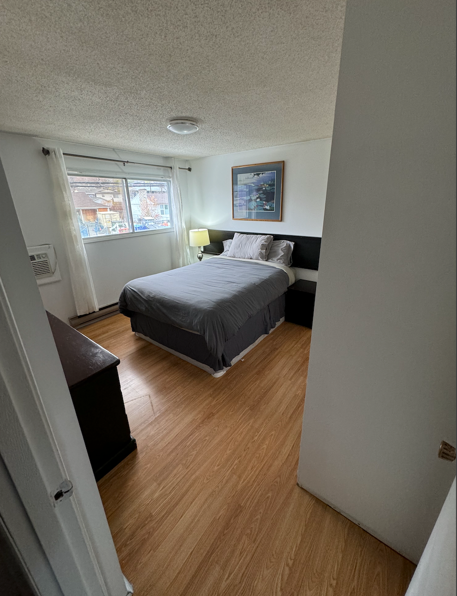 A bedroom with a bed , dresser , nightstand and window.