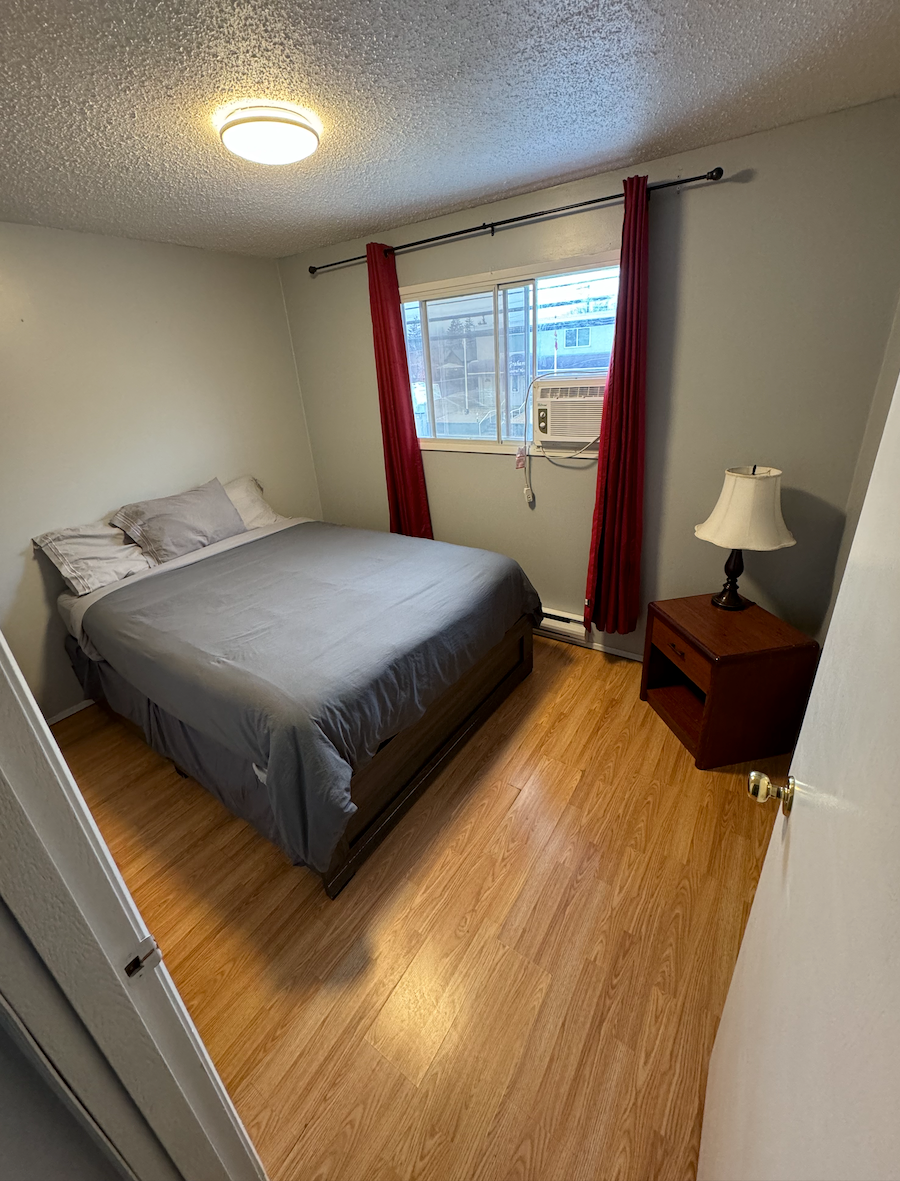 A bedroom with a bed , nightstand , lamp and window.