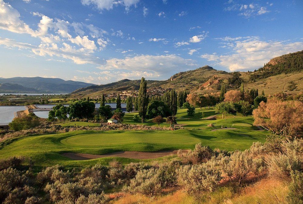 A golf course surrounded by mountains and trees with a lake in the background.