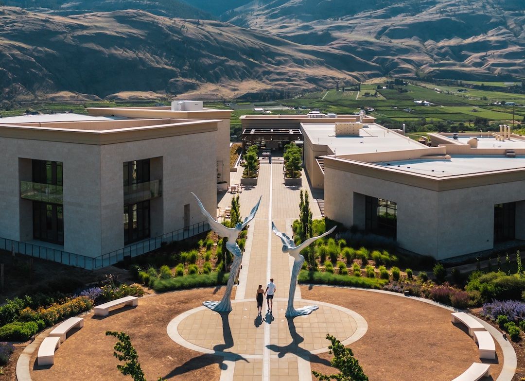 An aerial view of a couple walking in front of a building with mountains in the background.