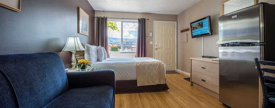 A hotel room with two beds , a couch , a television and a refrigerator.