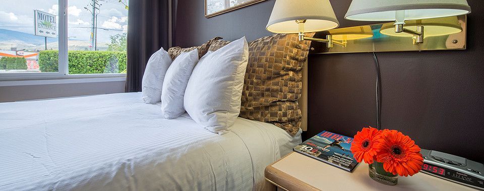 A hotel room with a bed , two lamps and a vase of flowers on the nightstand.