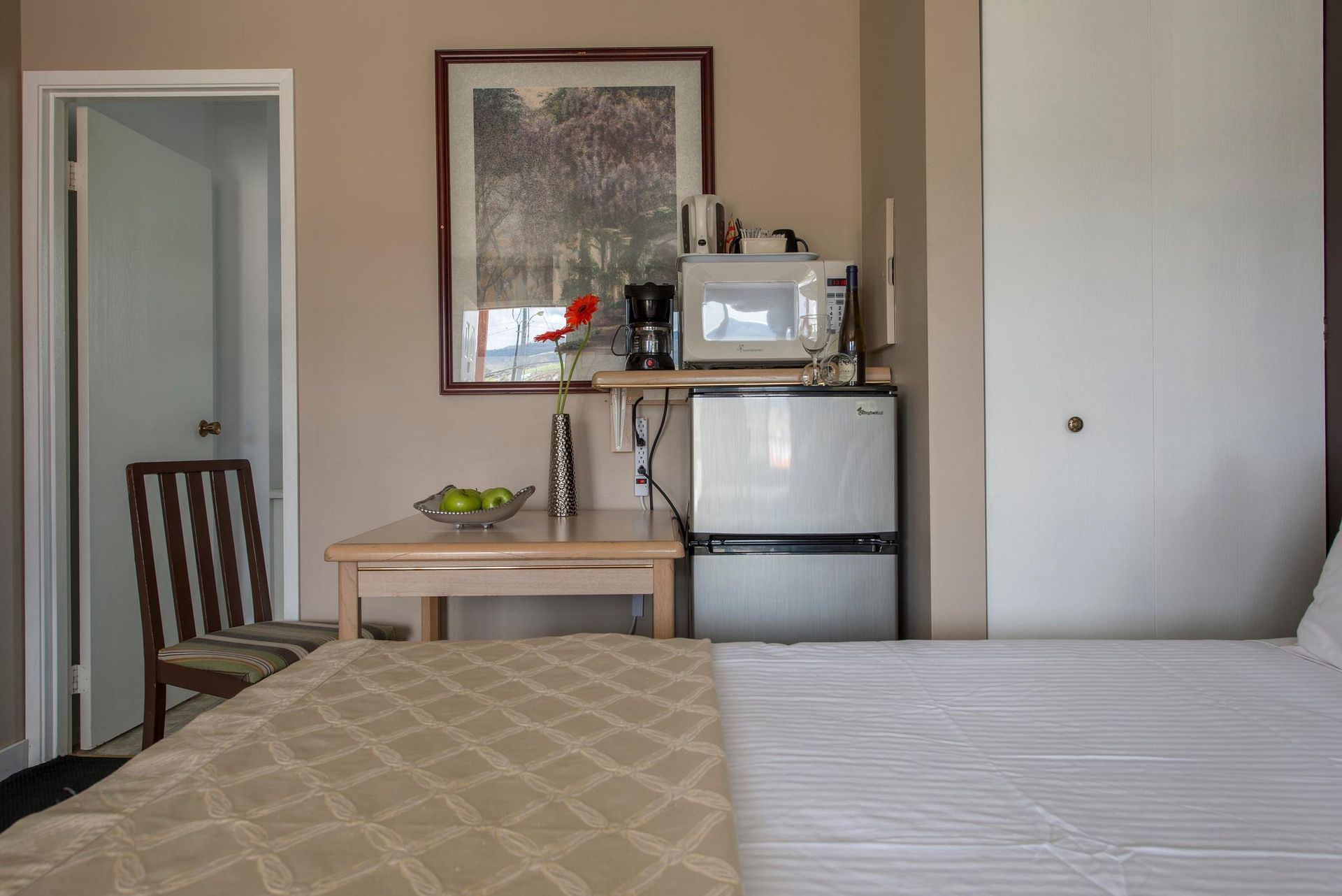A hotel room with a bed , table , chair and refrigerator.