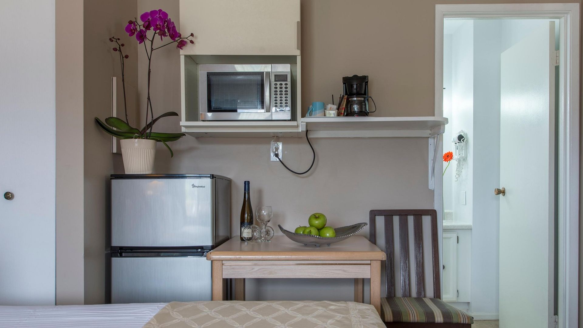 A bedroom with a table , chair , refrigerator and microwave.