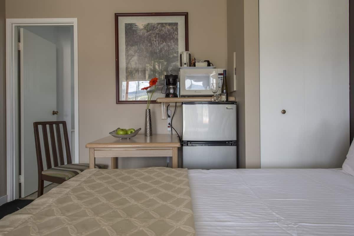 A hotel room with a table , chair , refrigerator and microwave.