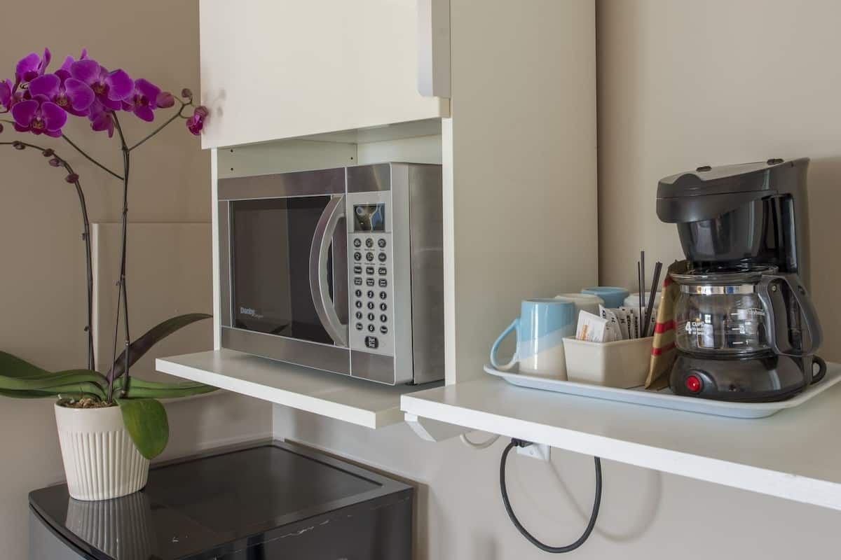 A microwave and coffee maker are on a shelf in a kitchen.