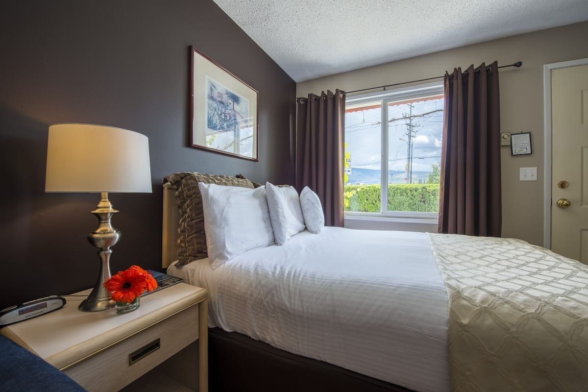 A bedroom with a bed , nightstand , lamp and window