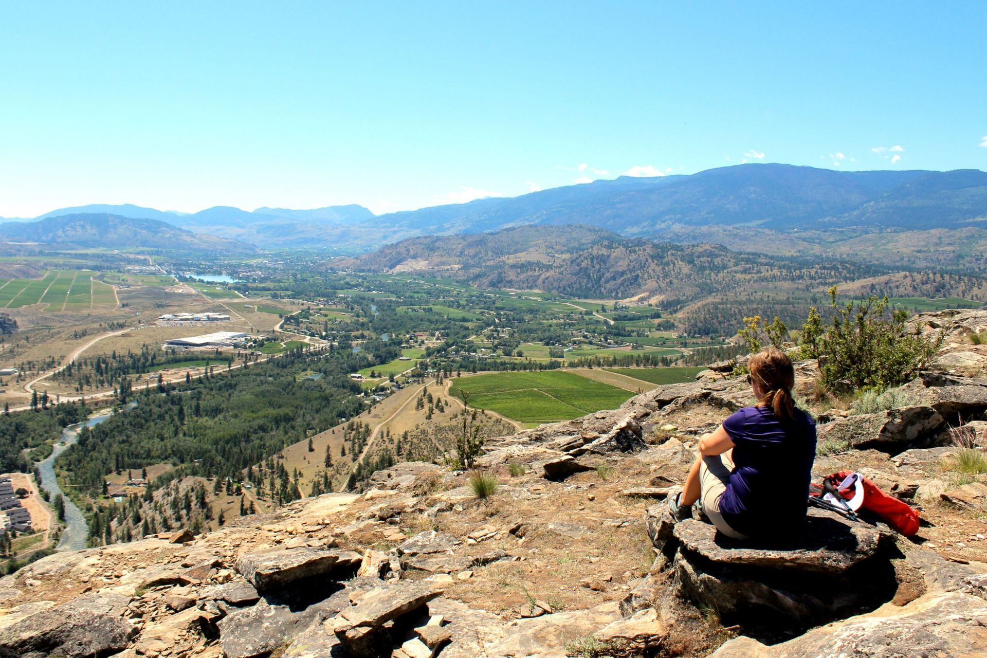 A woman is sitting on a rock overlooking a valley.