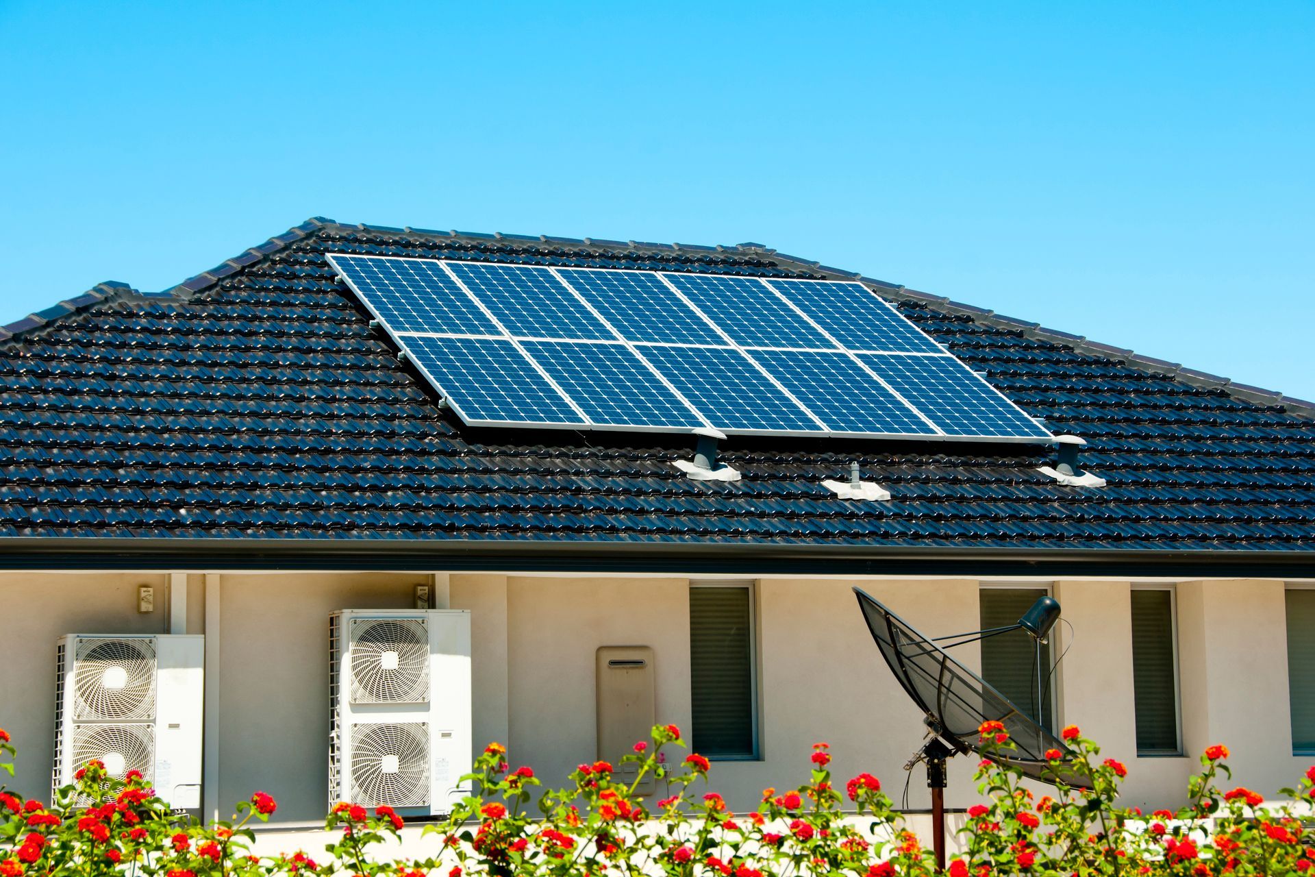 Solar panels on a residential roof, generating renewable energy. Blue sky, black roof, beige house.